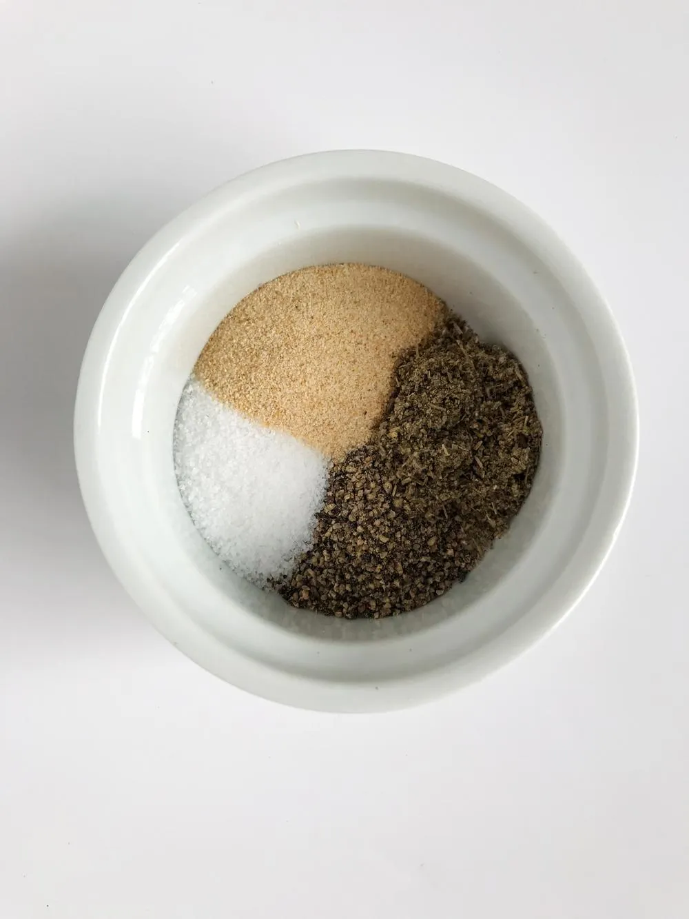 a small white bowl filled with spices like Dried Oregano, Rubbed Sage, Celery Salt, Dried Marjoram, Salt, Onion and Garlic Powder