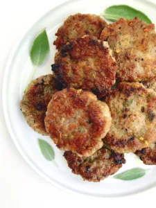 Maple-Sage Breakfast Patties on a plate surrounded by fresh sage.