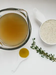 a measuring cup of homemade bone broth next to a half cup of jasmine rice and a sprig of thyme