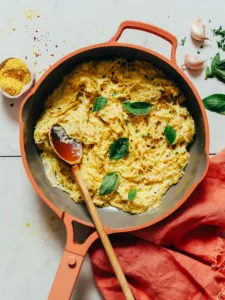 a red skillet of one pot spaghetti squash alfredo topped with fresh basil leaves and a wooden spoon