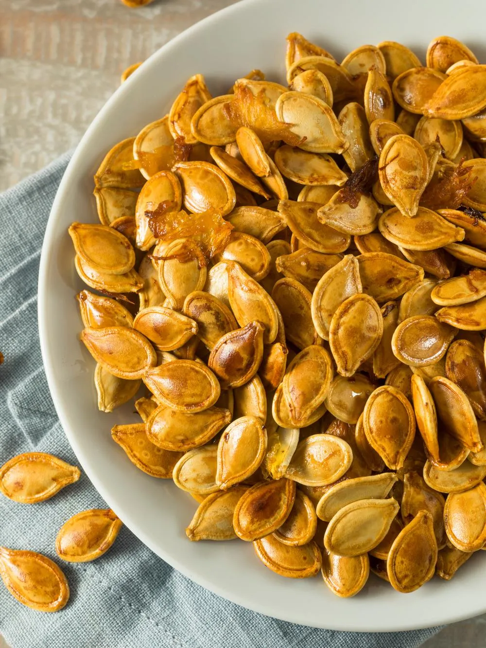 a white bowl filed with roasted butternut squash seeds sitting on a table with a blue cloth