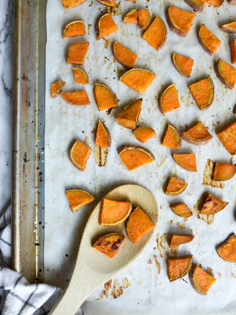 a baking sheet with parchment paper with roasted sweet potatoes cubes and a wooden spoon