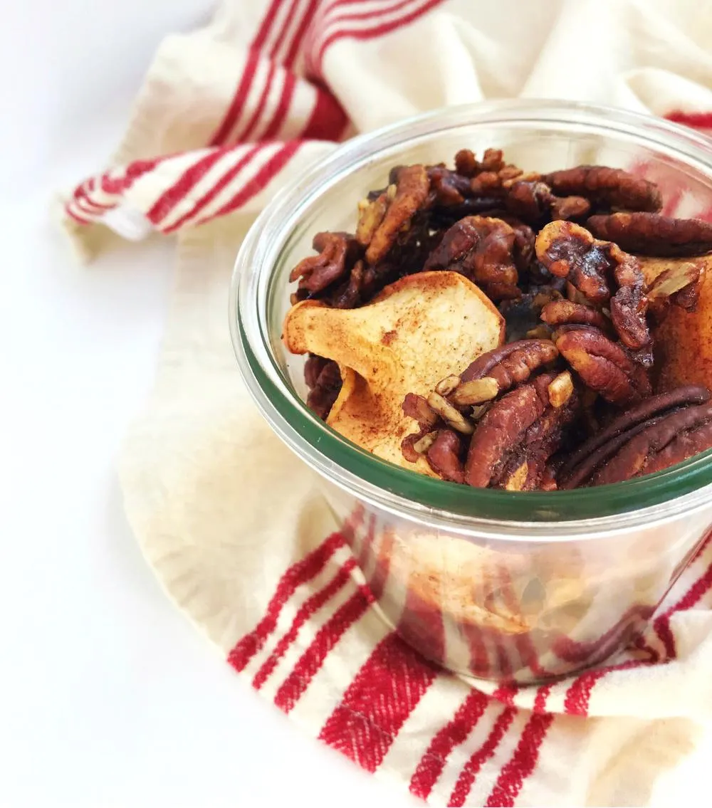 A jar of grain-free cinnamon apple granola, on top of a beige tea towel with red stripes.