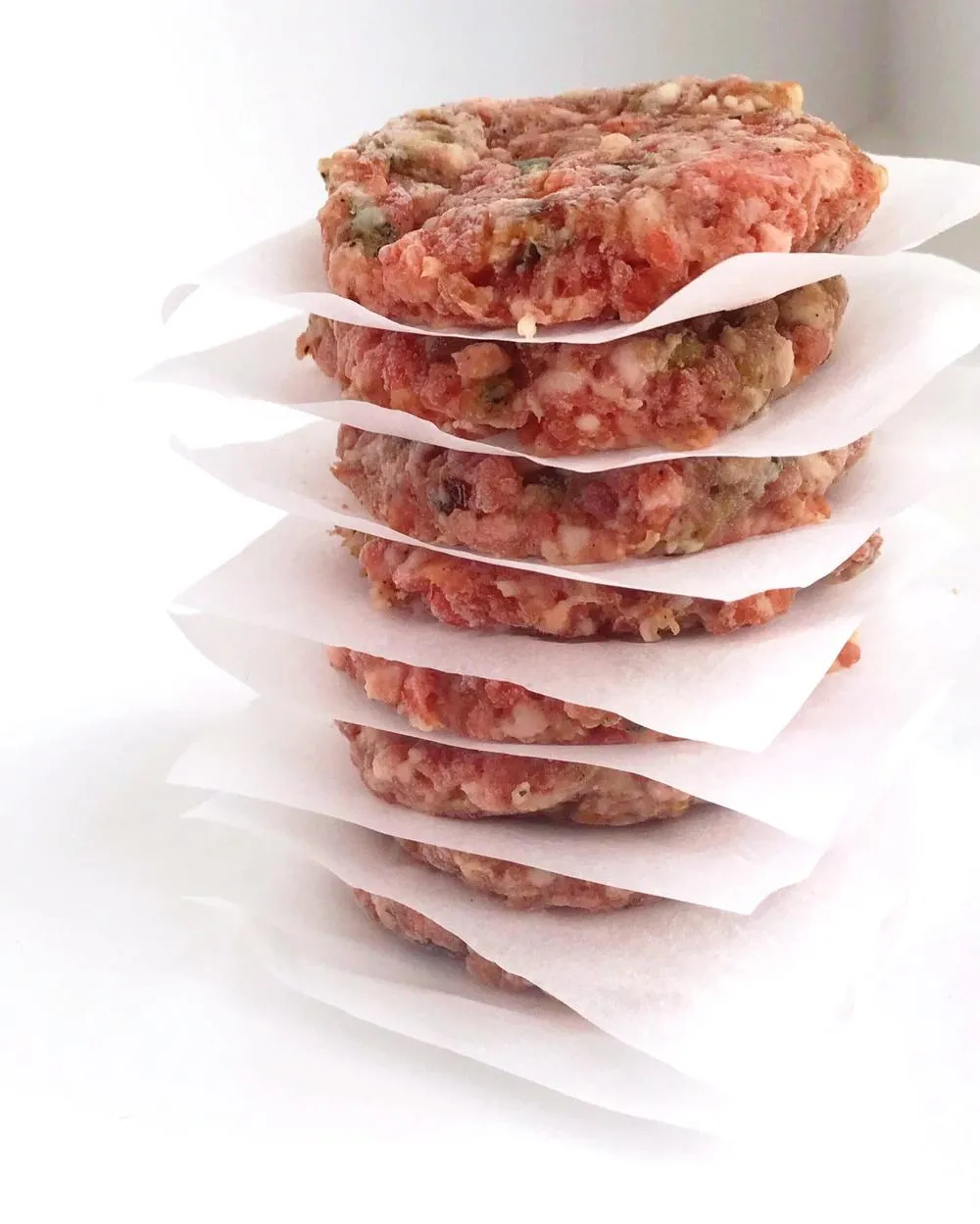 Stack of prepped Maple-Sage Breakfast Patties with parchment paper in between each patty.