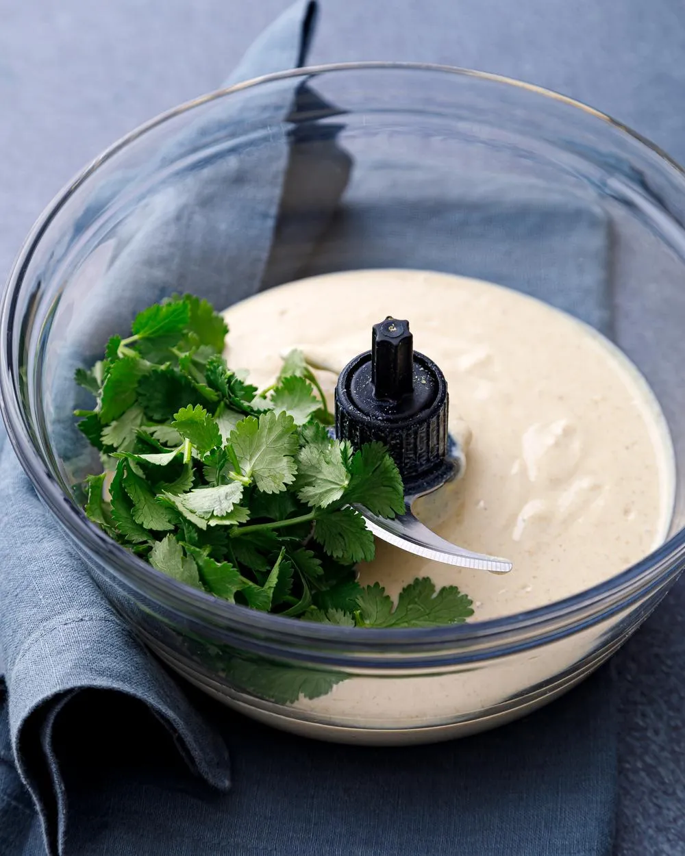 a glass bowl full of creamy and delicious tofu queso with a handful of fresh cilantro on top