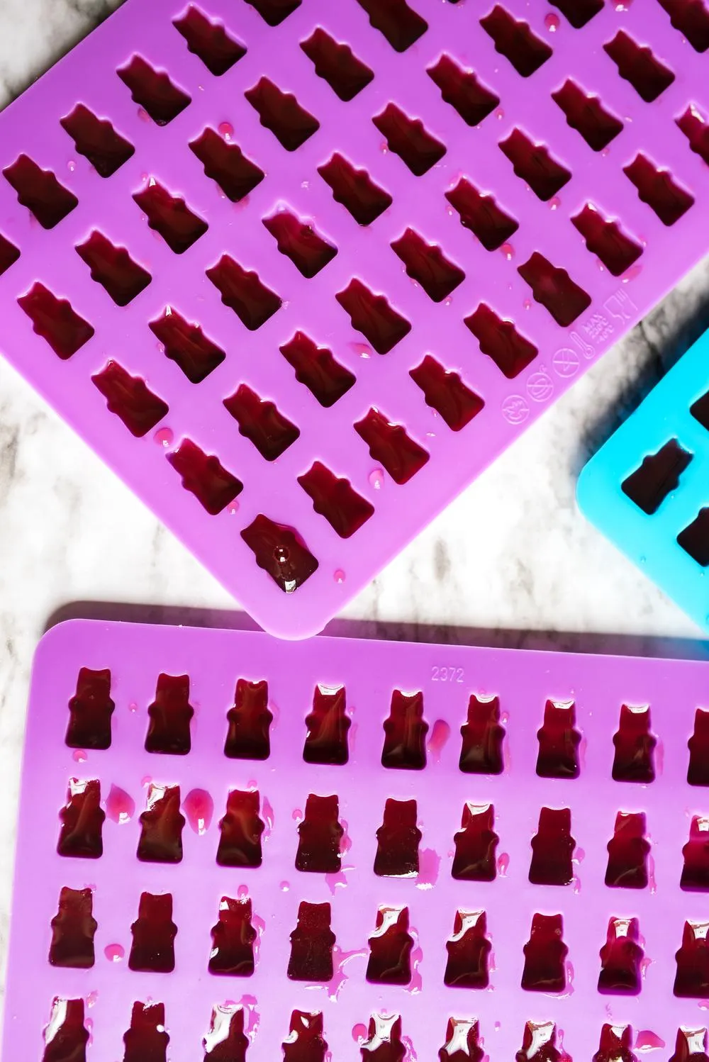 two purple and one blue gummy bear molds filled with vegan grape mix to make vegan gummy bears