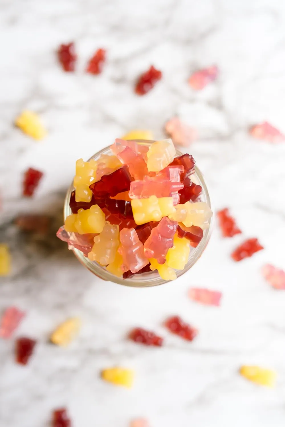 a small jar full of colorful vegan gummy bears with some spilled out and around the jar