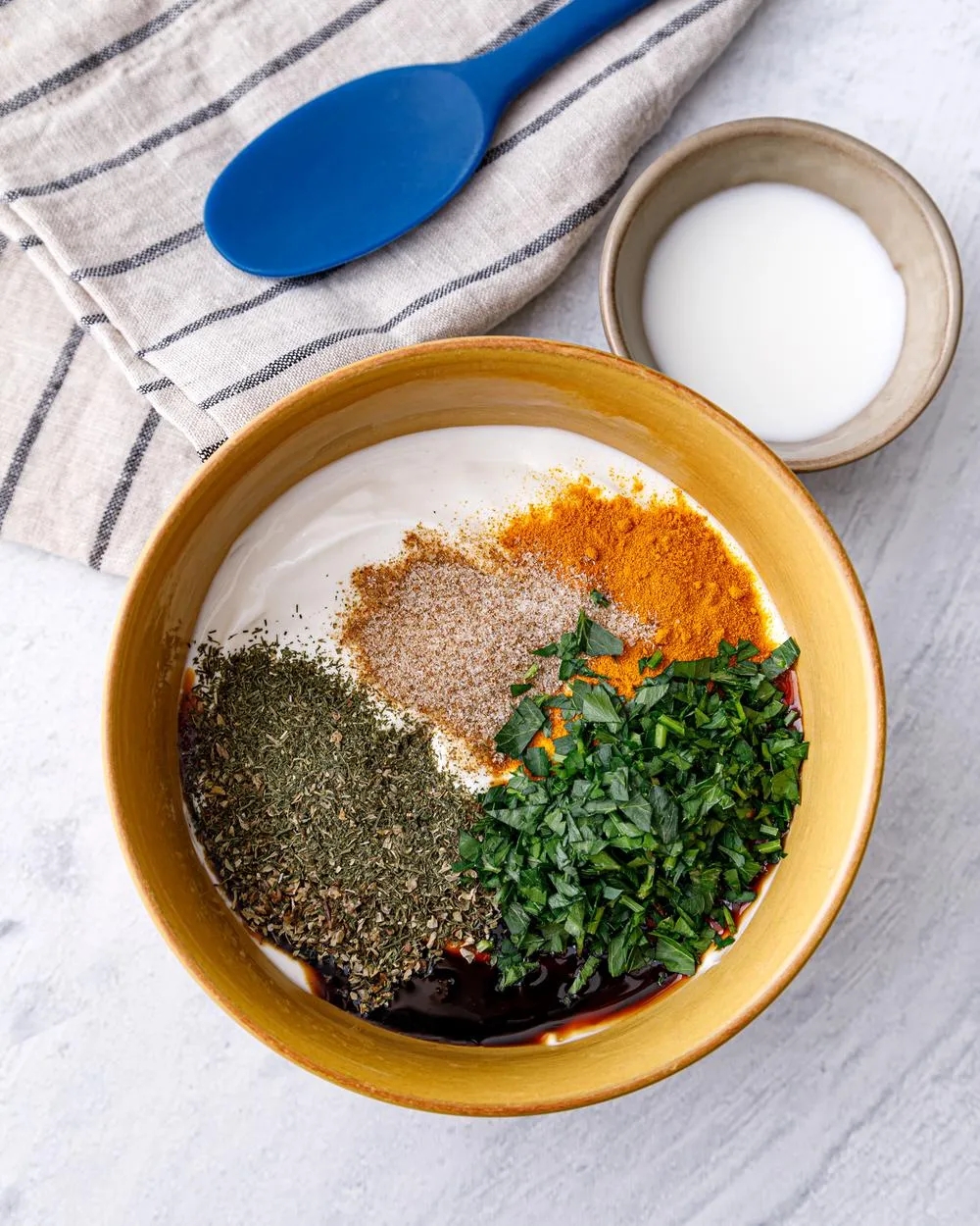 Ingredients for chicken wing dipping sauce in a bowl on a table including sourcream, honey, parsley, dill, and marjoram