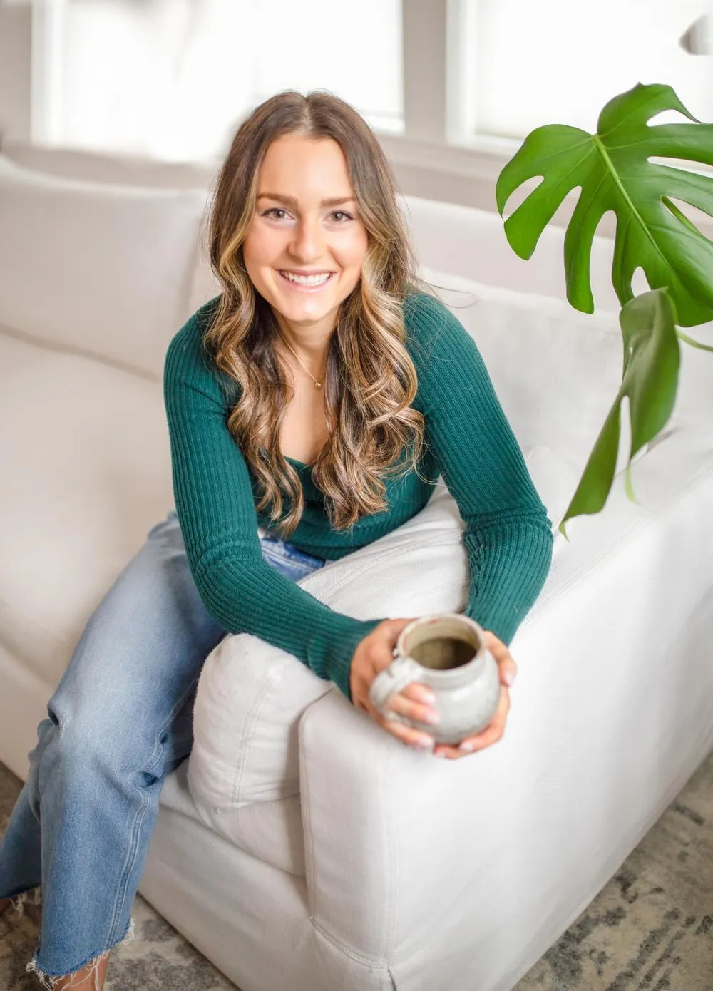 a woman dietitian sitting on a white couch holding a cup of hot tea with a plant in the background