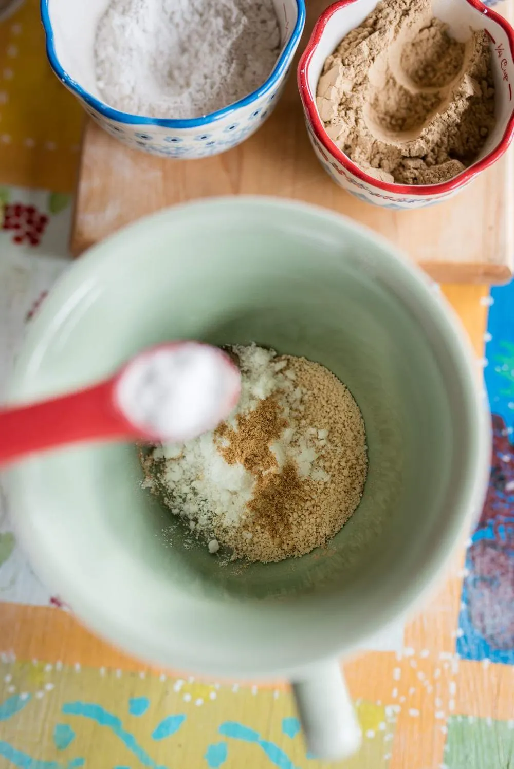 a green mug filled with dry heartburn ginger tea ingredients and a red spoon full of white powder in the foreground