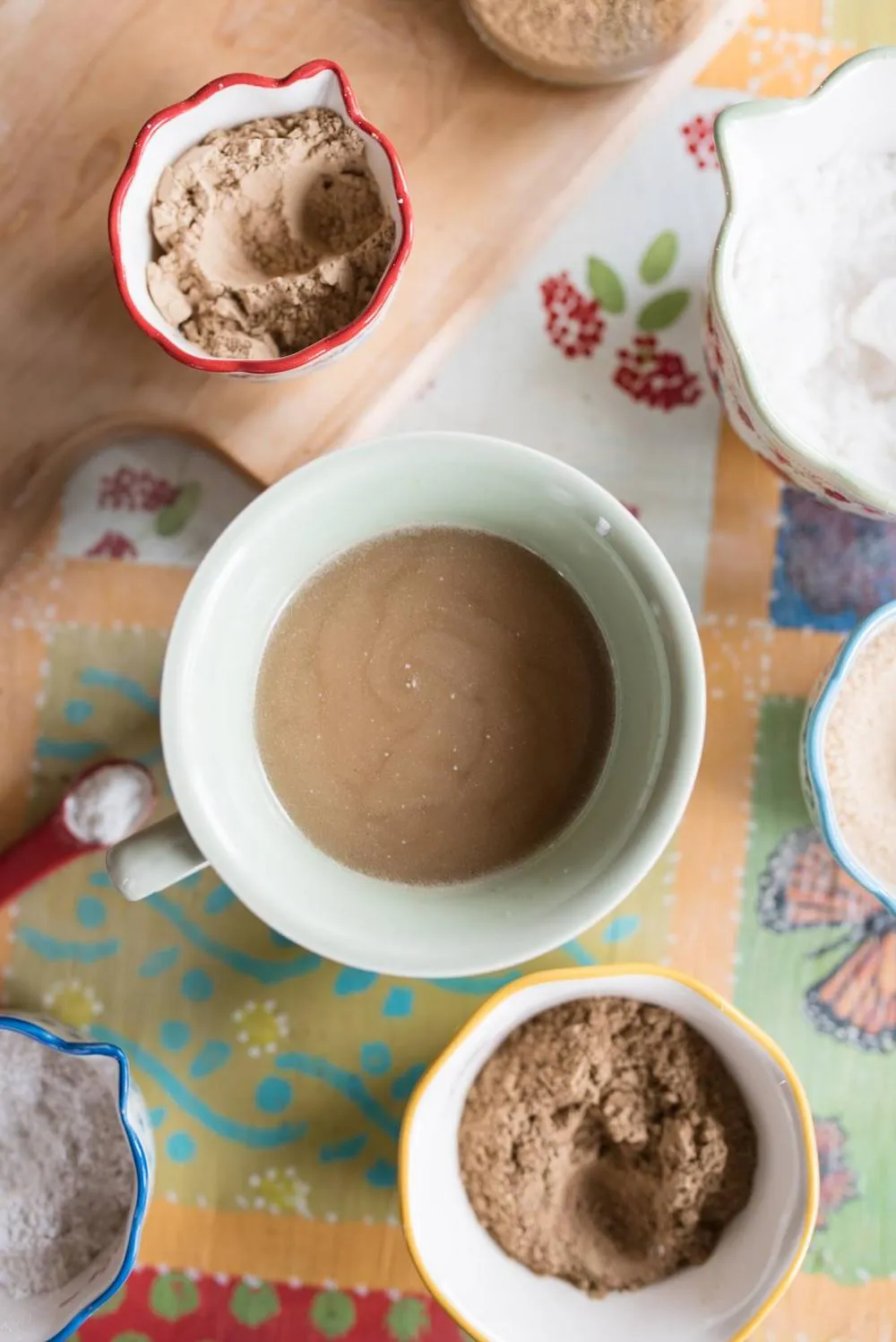 green mug filled with heartburn ginger tea surrounded by bowls of herbs