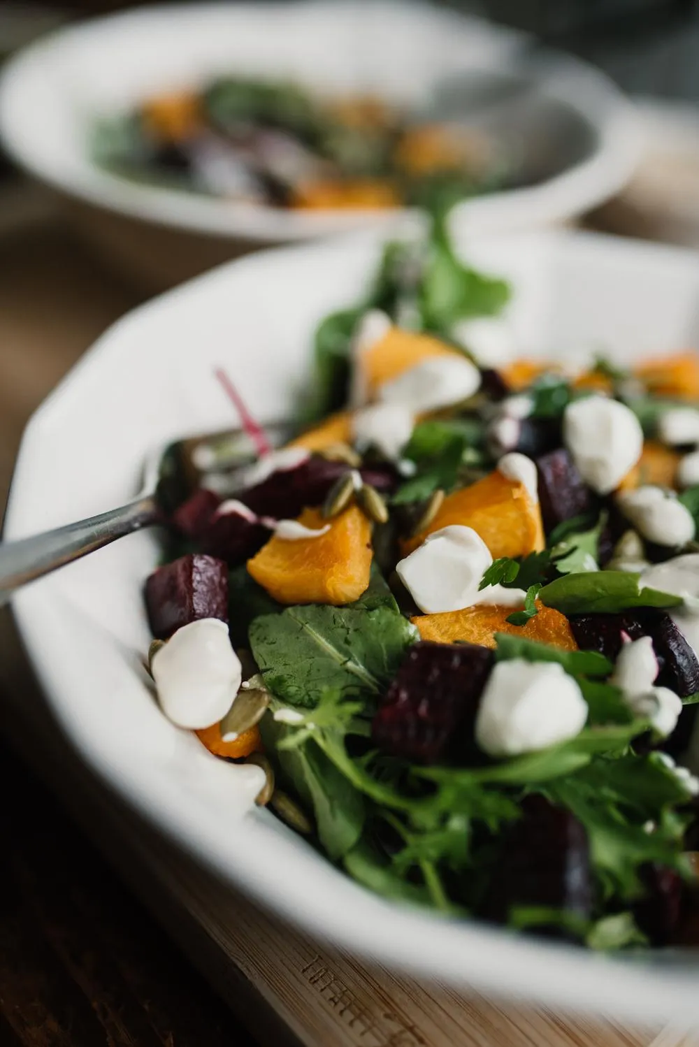 a white bowl of beetroot and butternut salad with a fork and a second salad behind it