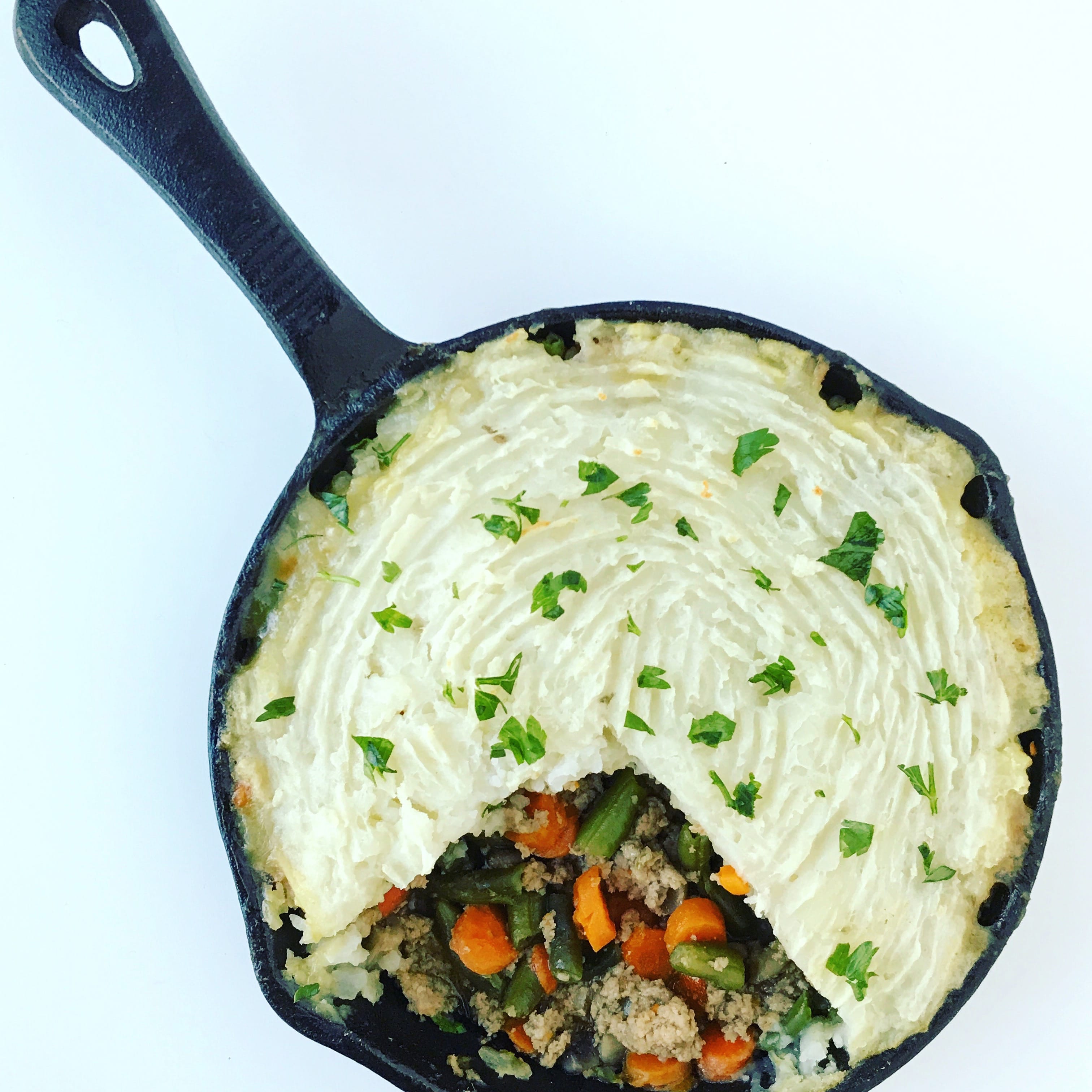 a cast iron skillet full of shepard's pie, topped with fresh chopped parsley