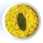 A brightly colored turmeric coconut rice in a small white ramekin topped with a single bay leaf