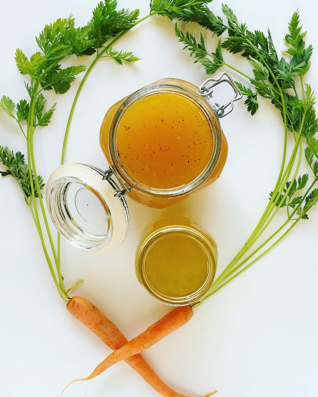 Jars of slow cooker chicken bone broth surrounded by carrots