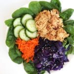 white bowl full of spinach, shredded carrots, purple cabbage, sliced cucumber, and slow cooker Asian honey chicken