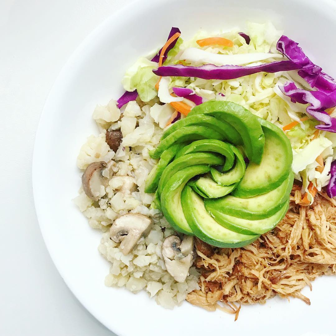 white bowl with slow cooker Asian honey chicken, cauliflower rice, mushrooms, cabbage, and an avocado styled like a rose