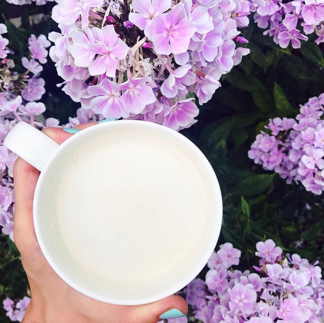 hand holding mug of tea in front of purple flowers