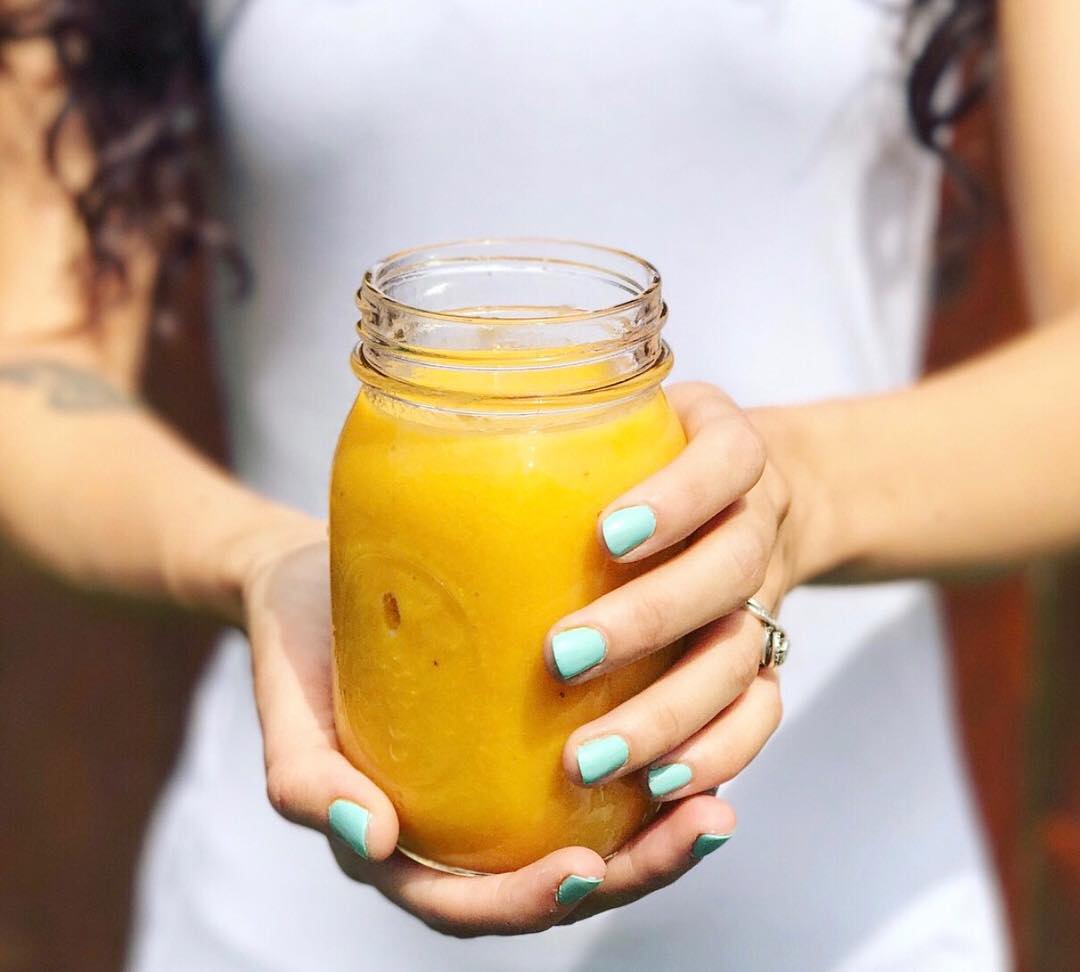 woman holding mason jar filled with a mango smoothie