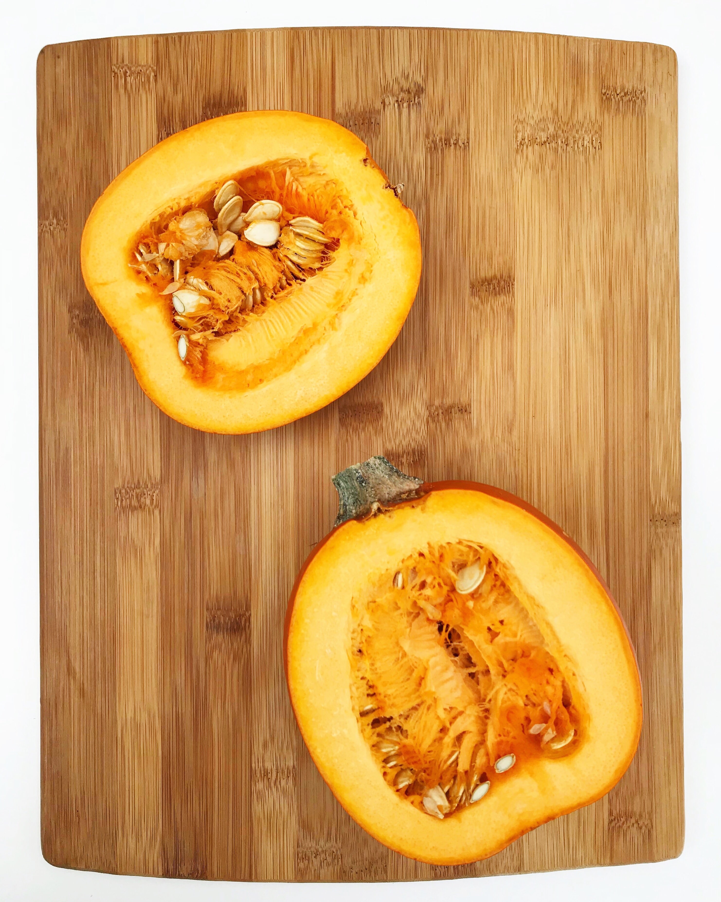 2 halves of a pumpkin on a wooden cutting board.
