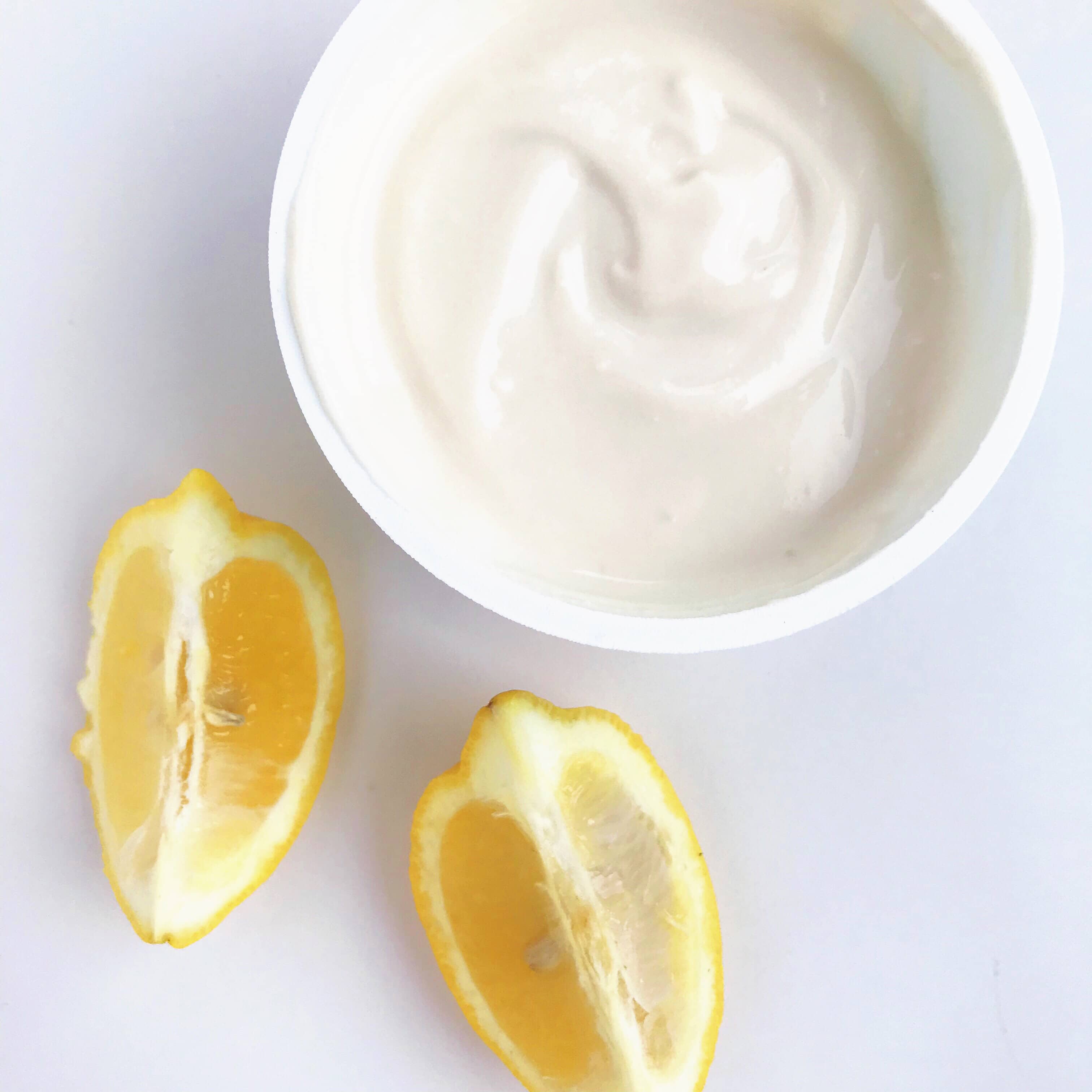 A cup of dairy-free almond-based yogurt next to two lemon wedges.
