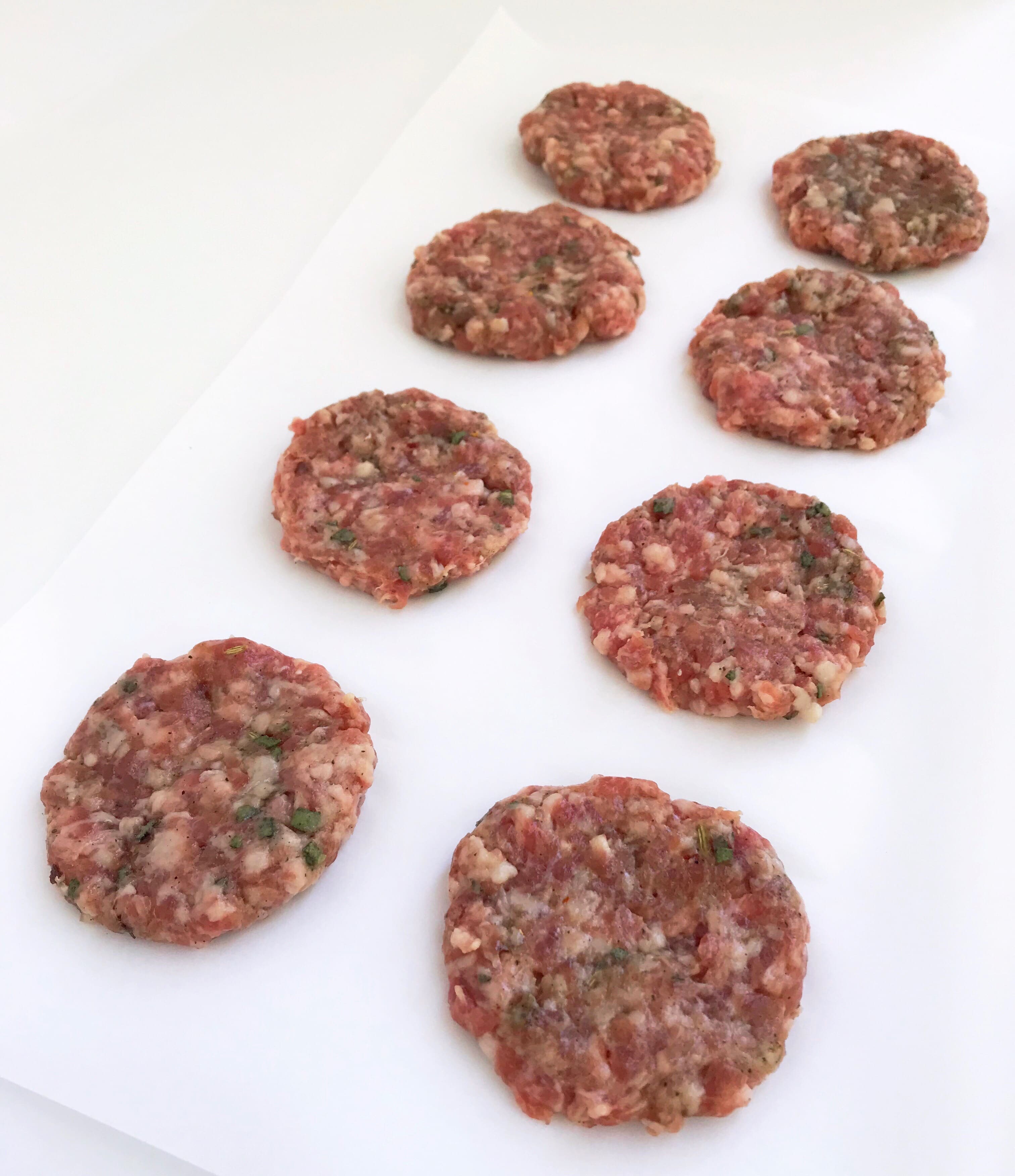 Pork sausage mixture molded into 8 patties on parchment paper.