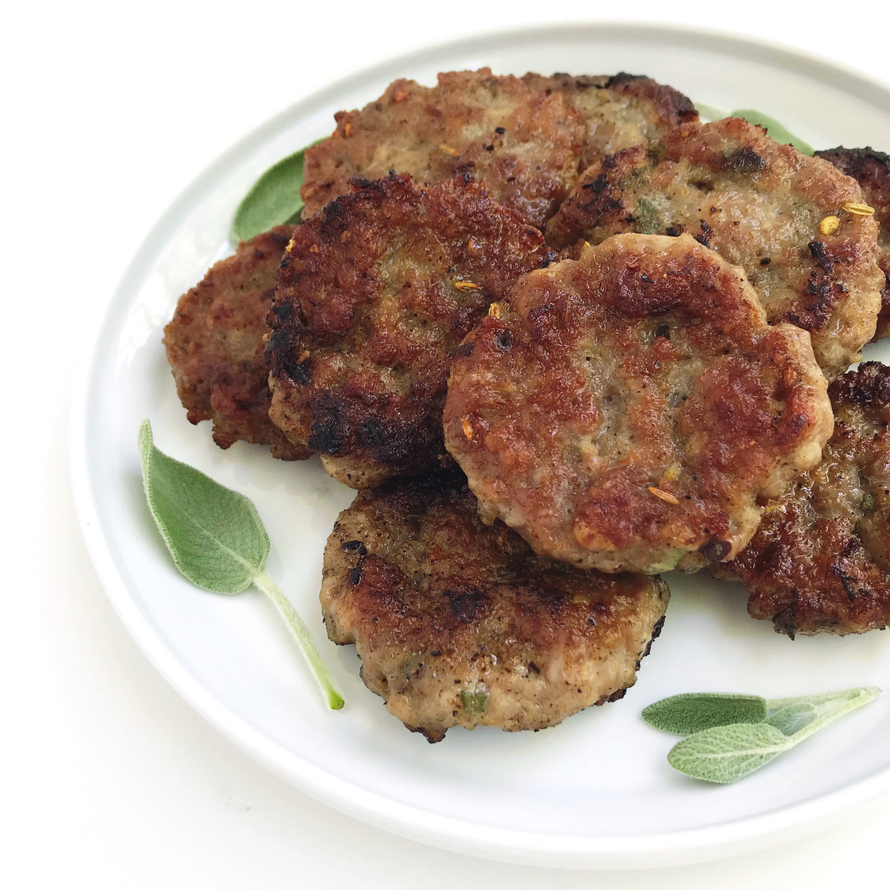 A plate of Maple-Sage Breakfast Patties, garnished with fresh sage leaves.