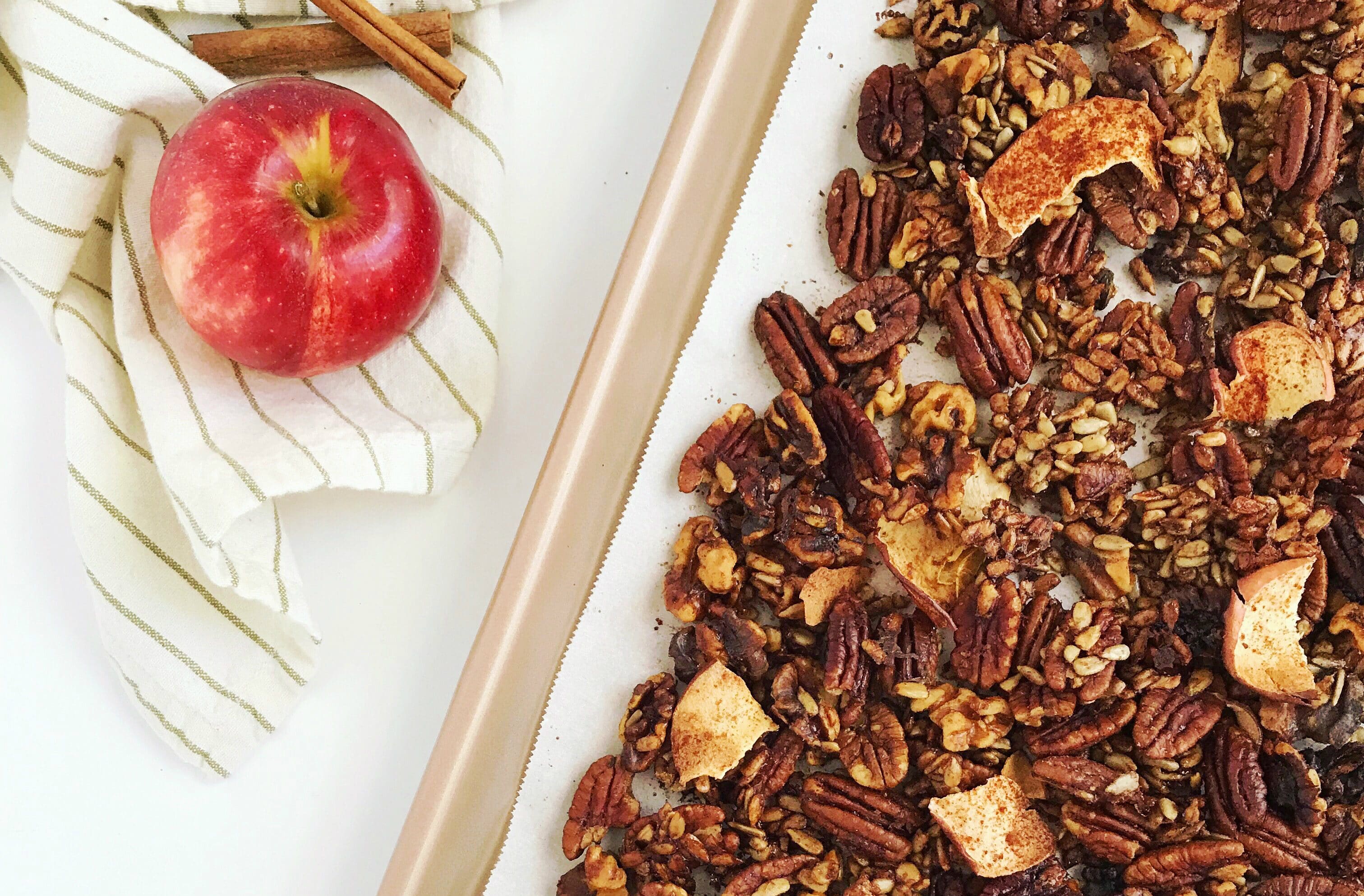 Grain-free cinnamon apple granola on a baking sheet with an apple and cinnamon sticks in the background.