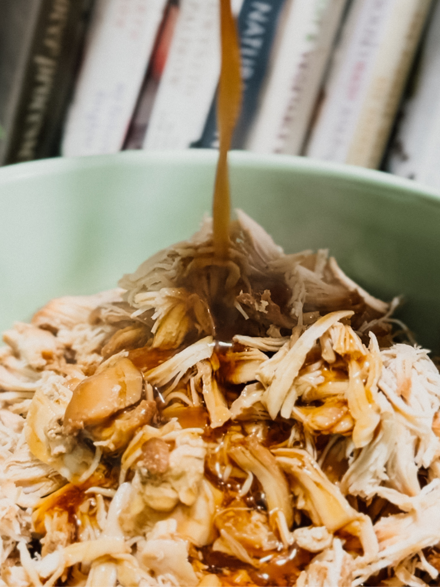 shredded slow cooker chicken in a green bowl with the Asian honey sauce being poured over it