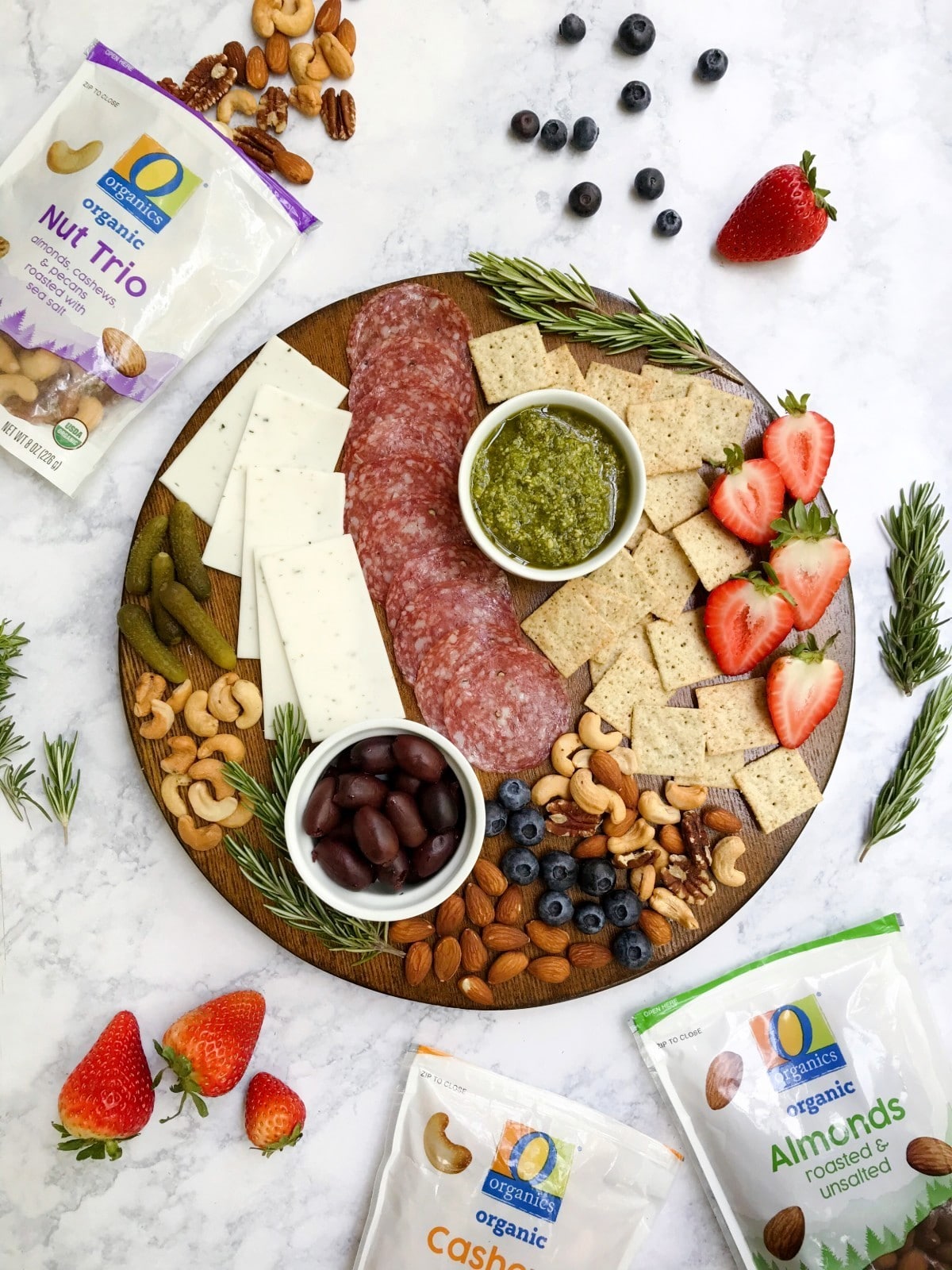 A charcuterie board that is gluten and dairy-free with a variety of ingredients such as meat, cheese, crackers, nuts, fruit, etc. Displaying O Organics Nuts in the background.