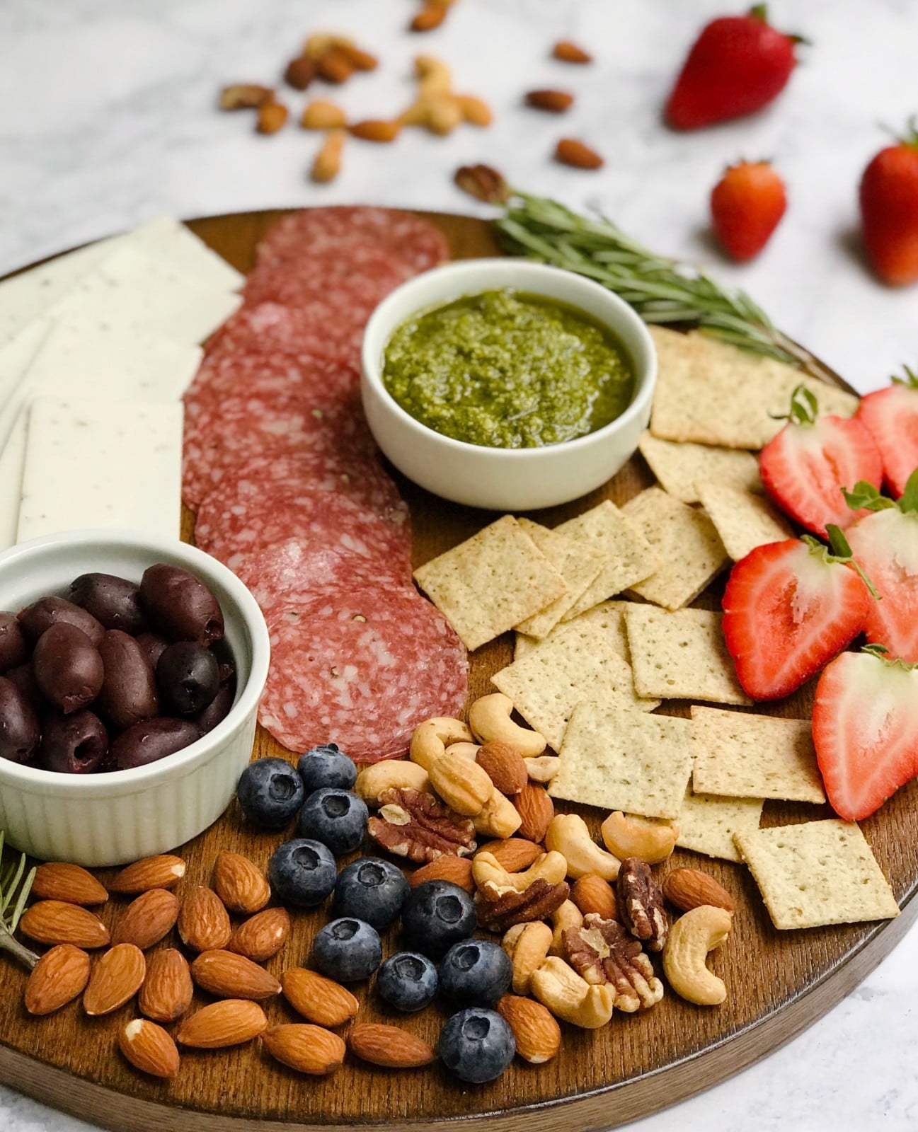 A gluten-free and dairy-free charcuterie board displaying meat, cheese, nuts, fruit, fresh herbs, crackers, olives, and pickles.