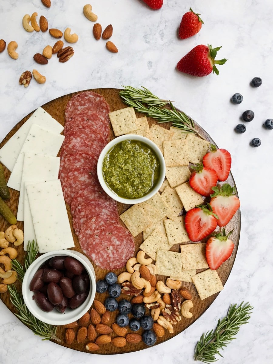 A charcuterie board that is gluten and dairy-free with a variety of ingredients such as meat, cheese, crackers, nuts, fruit, etc. Displaying O Organics Nuts in the background.