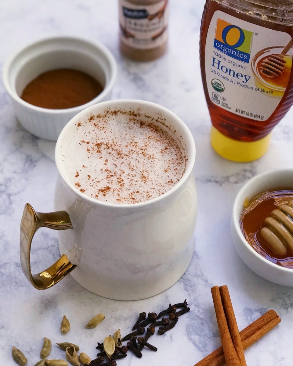 A cinnamon chamomile latte with honey, cinnamon, cardamom, and cloves in the background