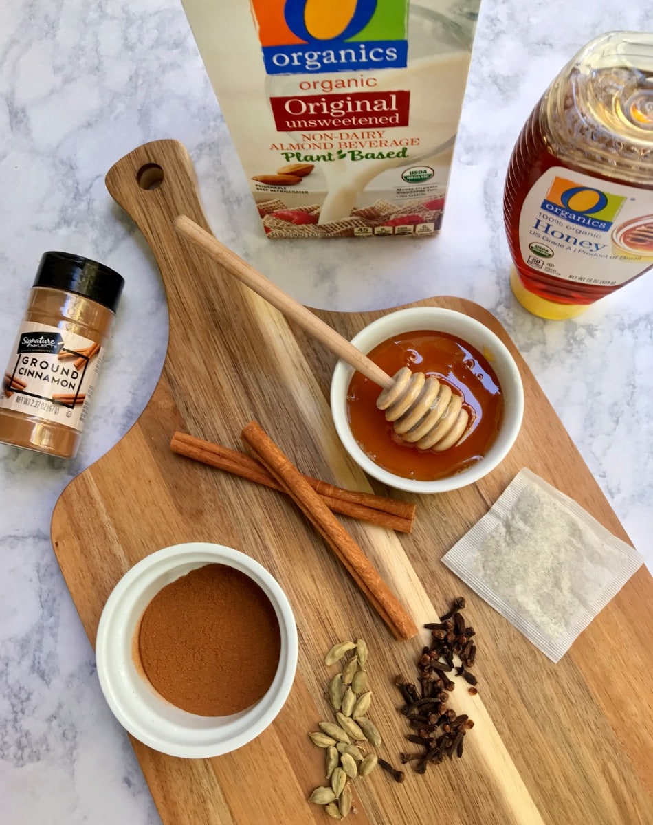 Ingredients spread out on a cutting board including Signature Select ground cinnamon, cinnamon sticks, cardamom pods, whole cloves, O Organics almond milk, O Organics honey, and a chamomile tea bag