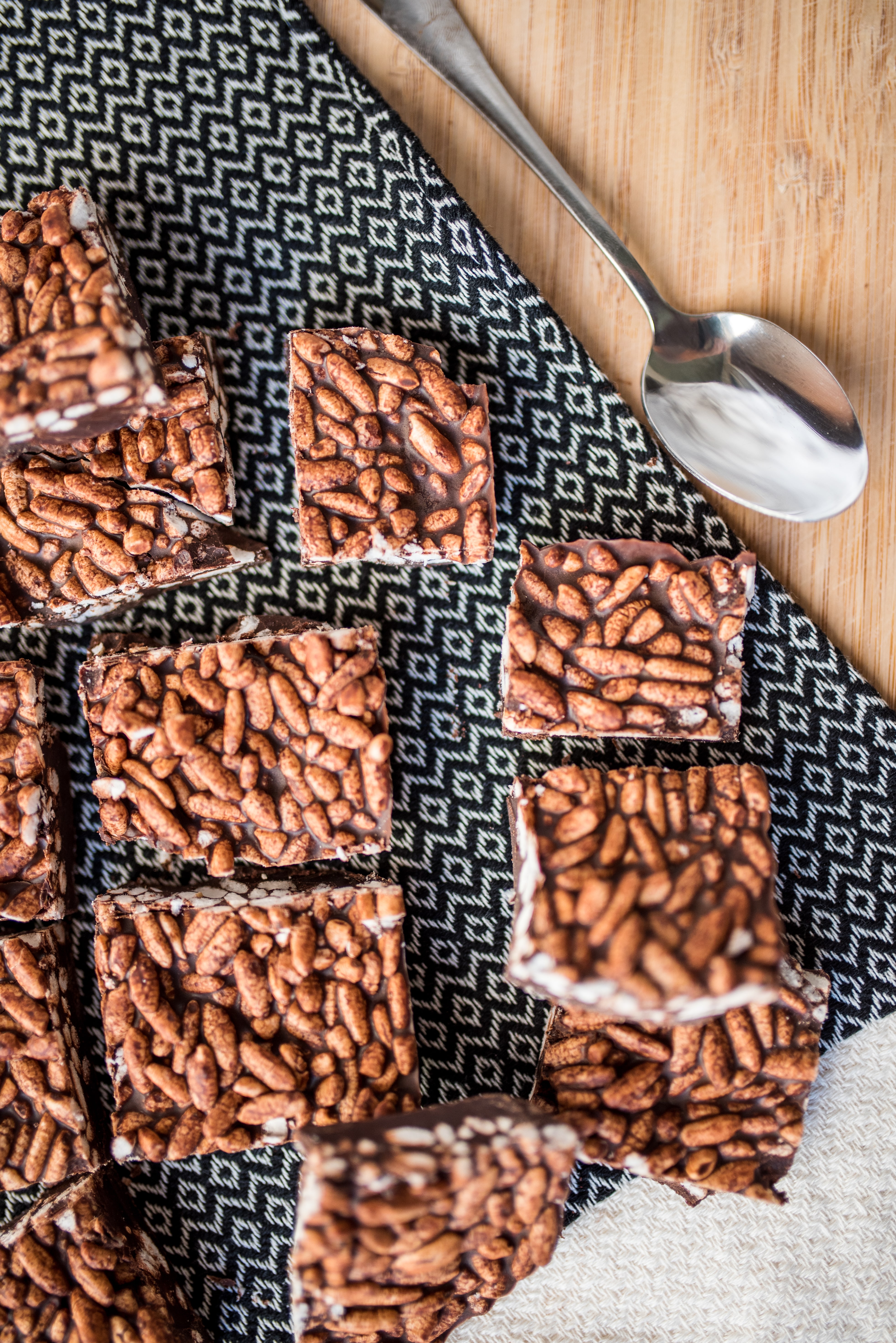 sliced sugar free, dairy free chocolate crunch bars on a cutting board with a black and white checked dishcloth and a silver spoon