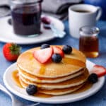 Stack of almond milk pancakes on a table with syrup, blueberry compote and a mug of hot tea on a table with a strawberry