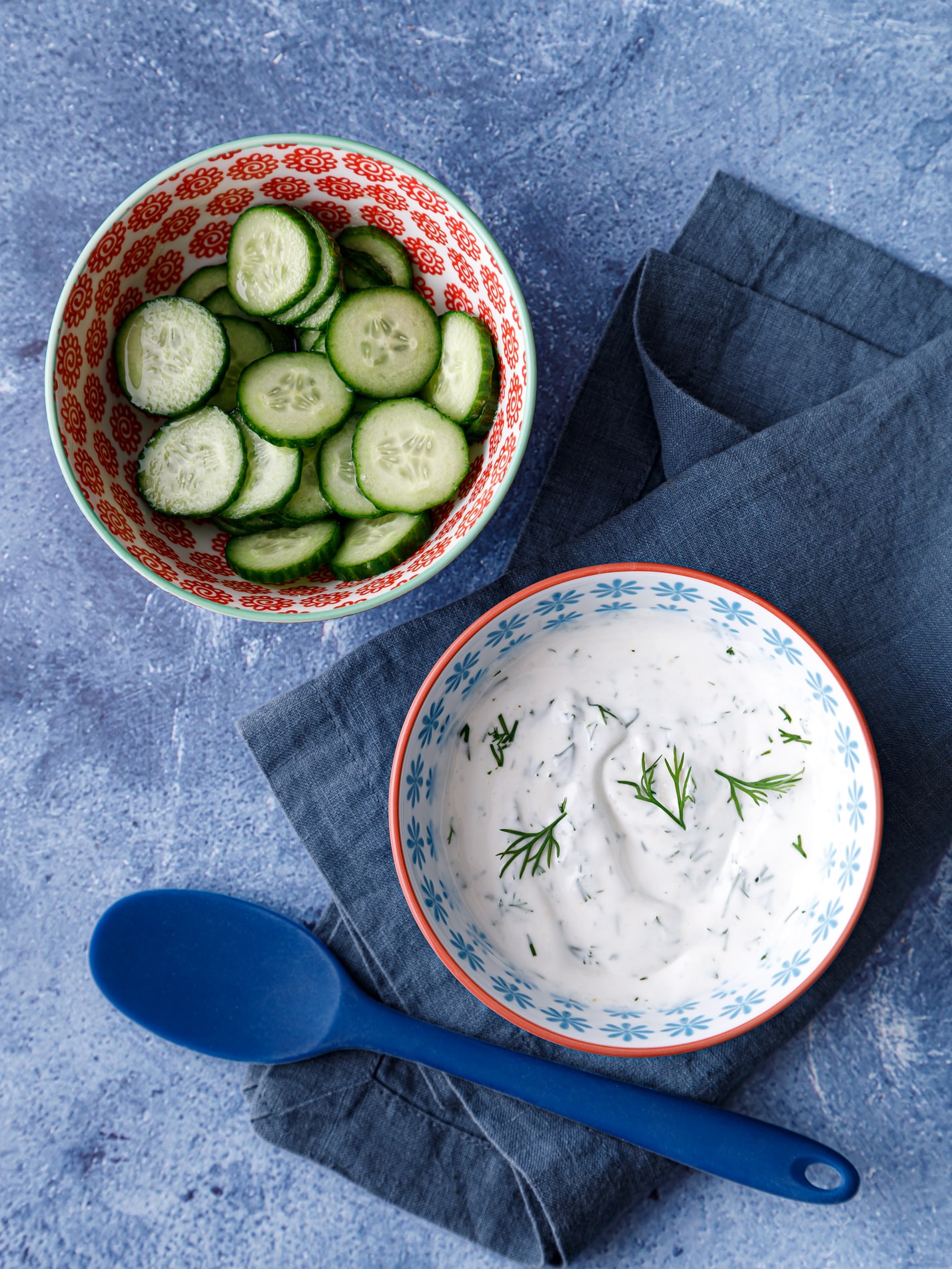 Two bowls on a table one filled with dairy free tzatziki sauce and one filled with slice cucumbers