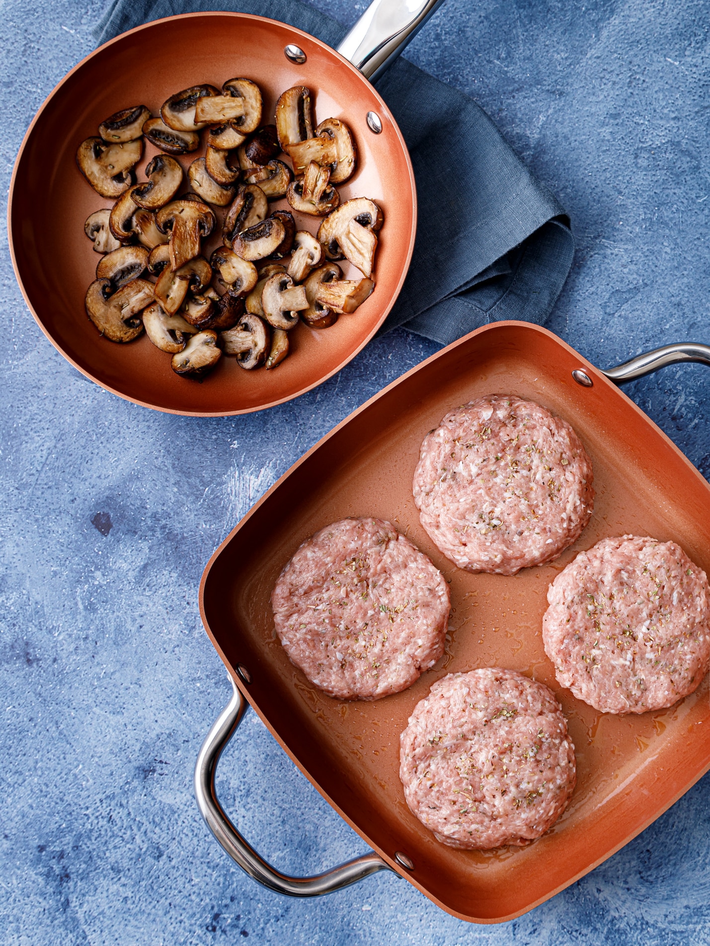 a pan with four turkey burgers patted out and ready to cook and a pan of sauteed mushrooms