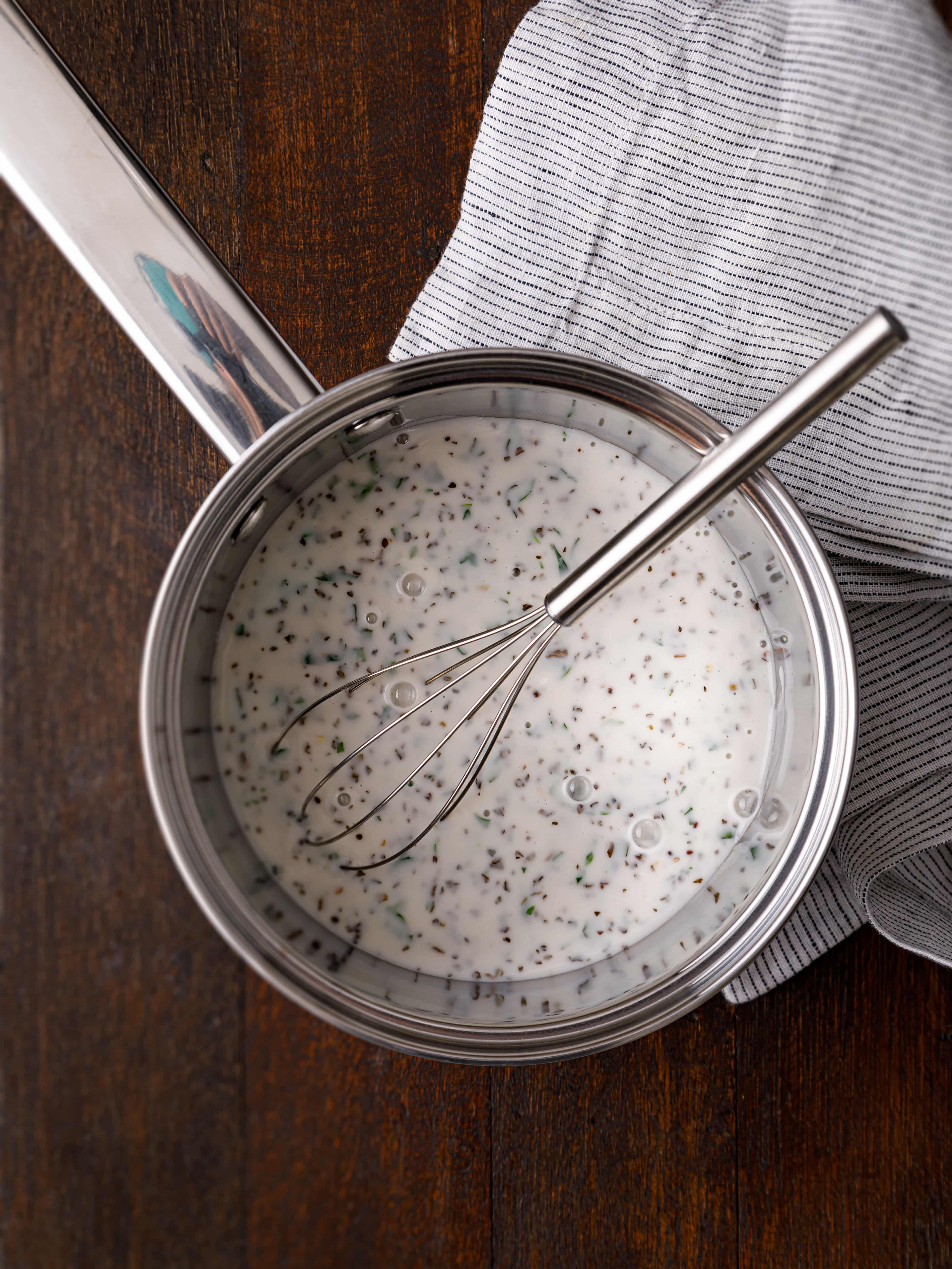 a pan of salad dressing with a whisk sitting on a brown table