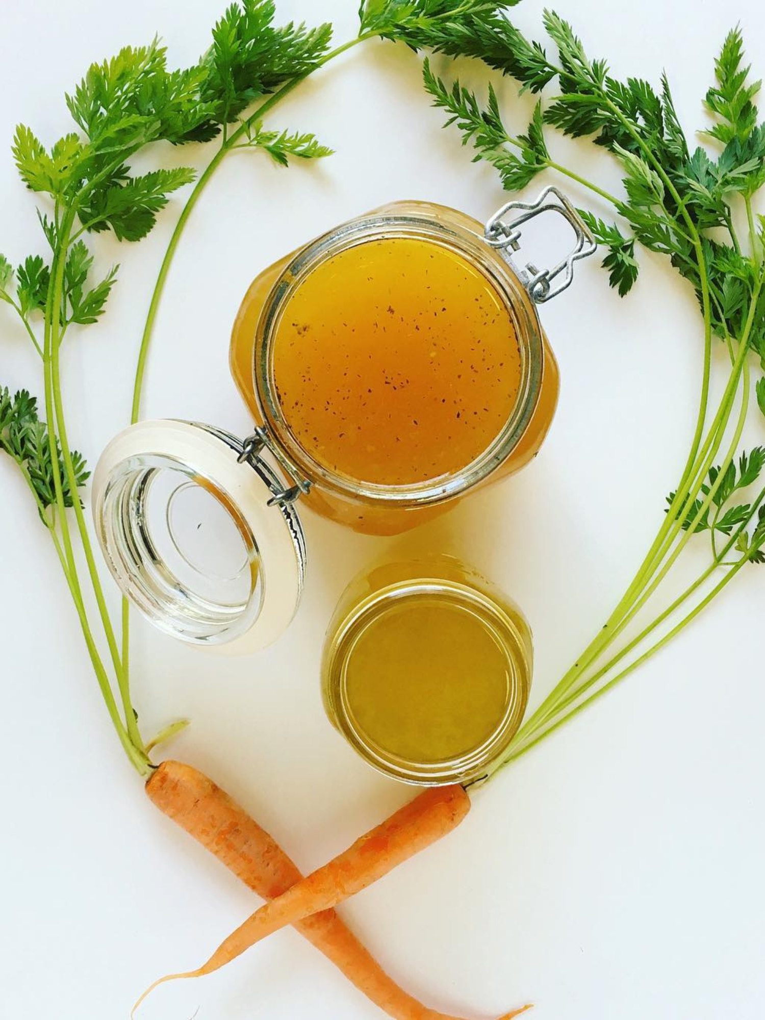 two jars full of slow cooker chicken broth surrounded by two small carrots