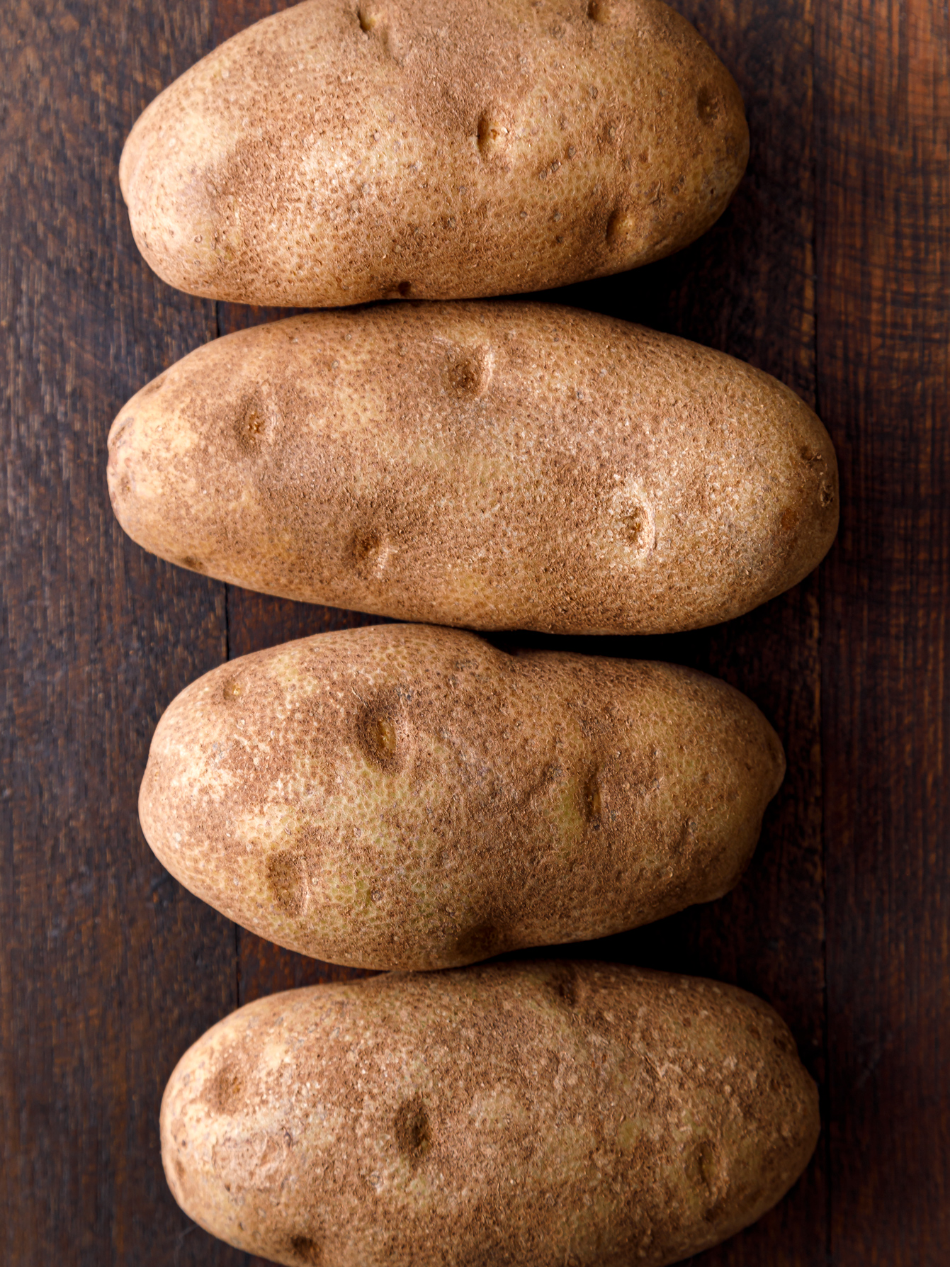 four large russett potatoes lined up ready for baking