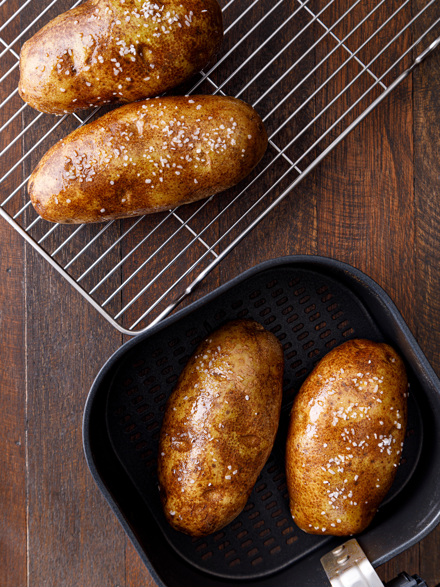 two russet potatoes sprayed lightly with olive oil in a skillet and two russet potatoes sprayed with olive oil on a cooling rack