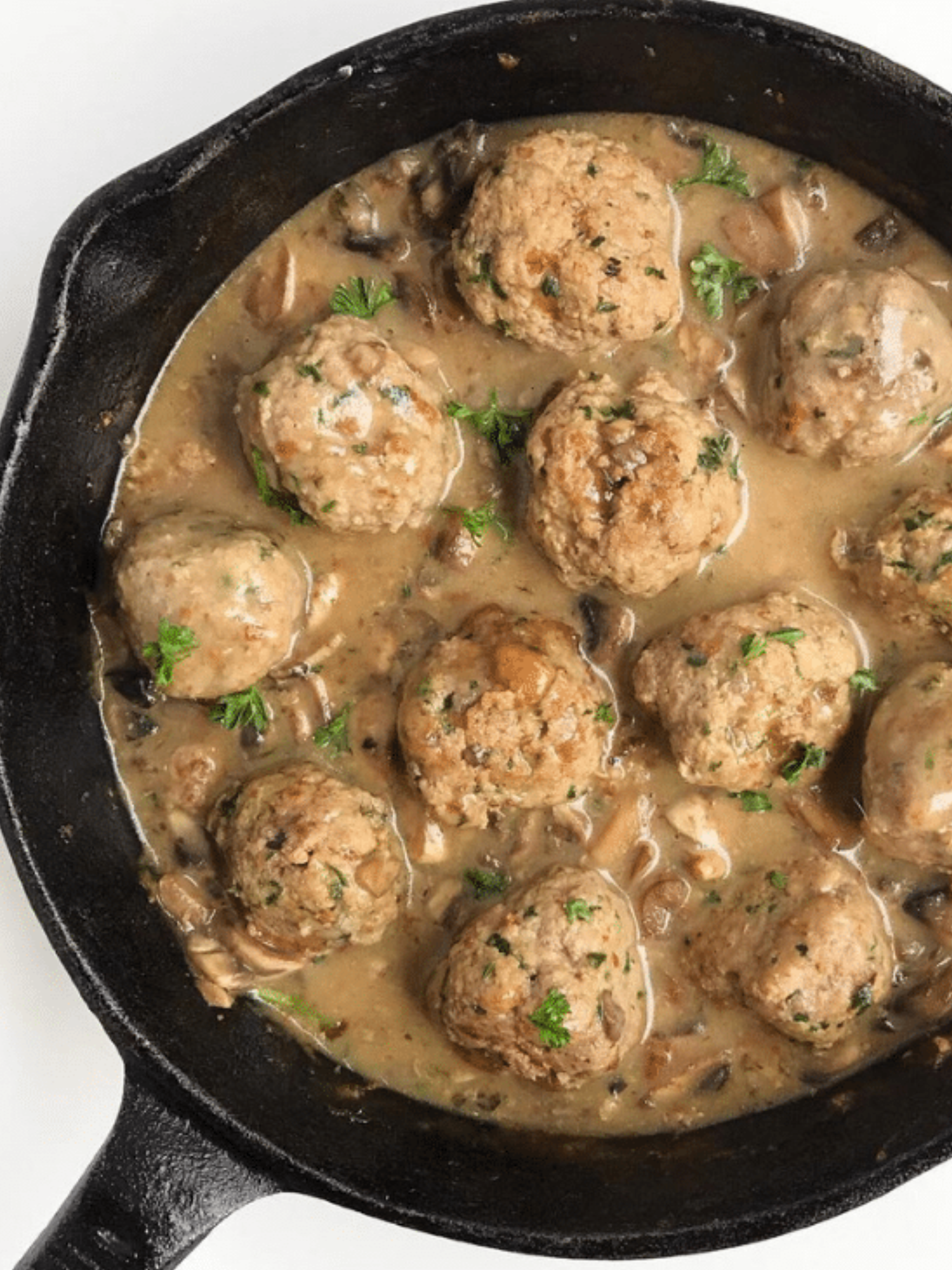 A cast iron skillet full of turkey meatballs and mushroom gravy