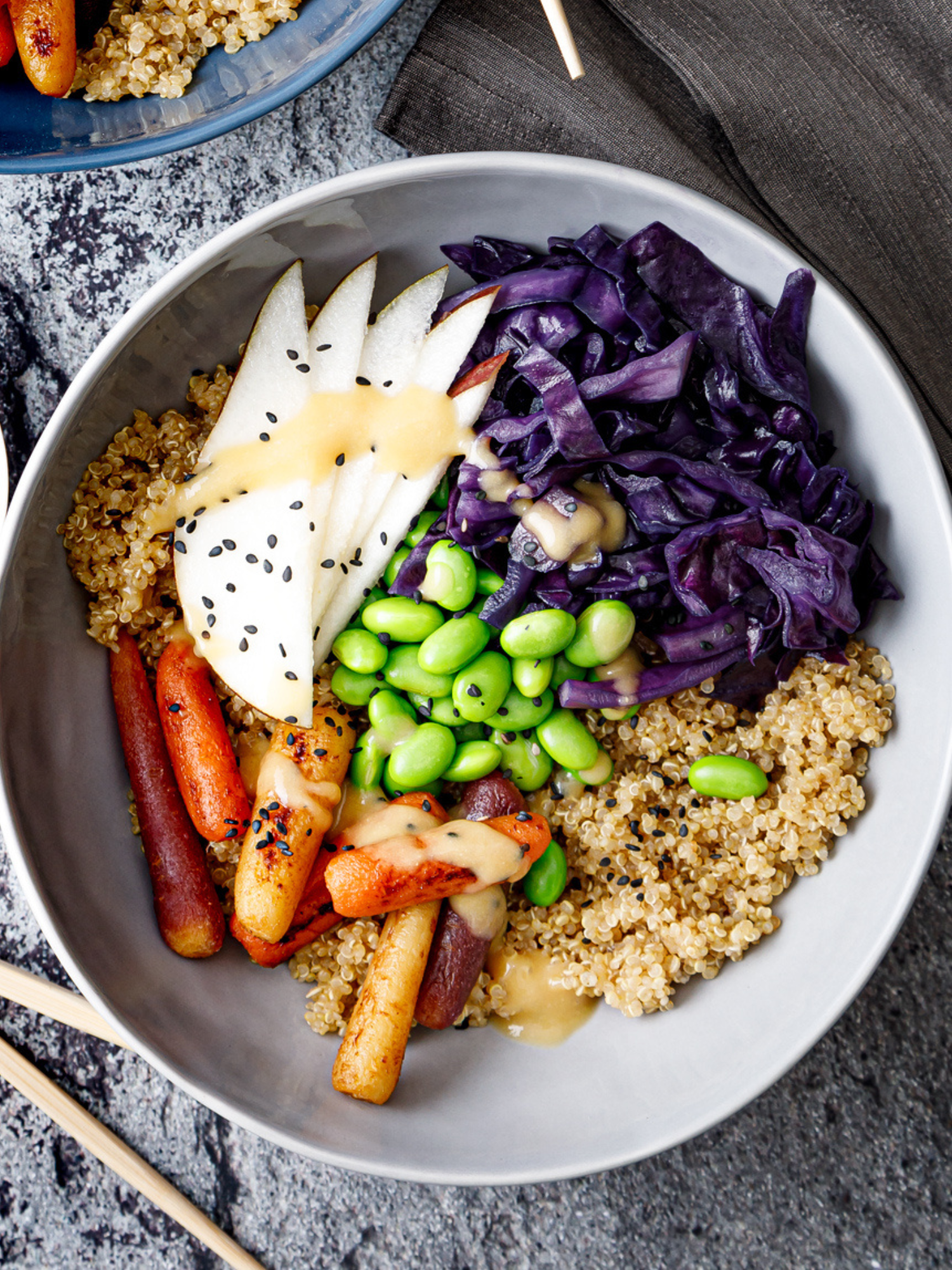 a white bowl of quinoa, shredded purple cabbage, pears, carrots and edamame drizzled with a pear, ginger sauce