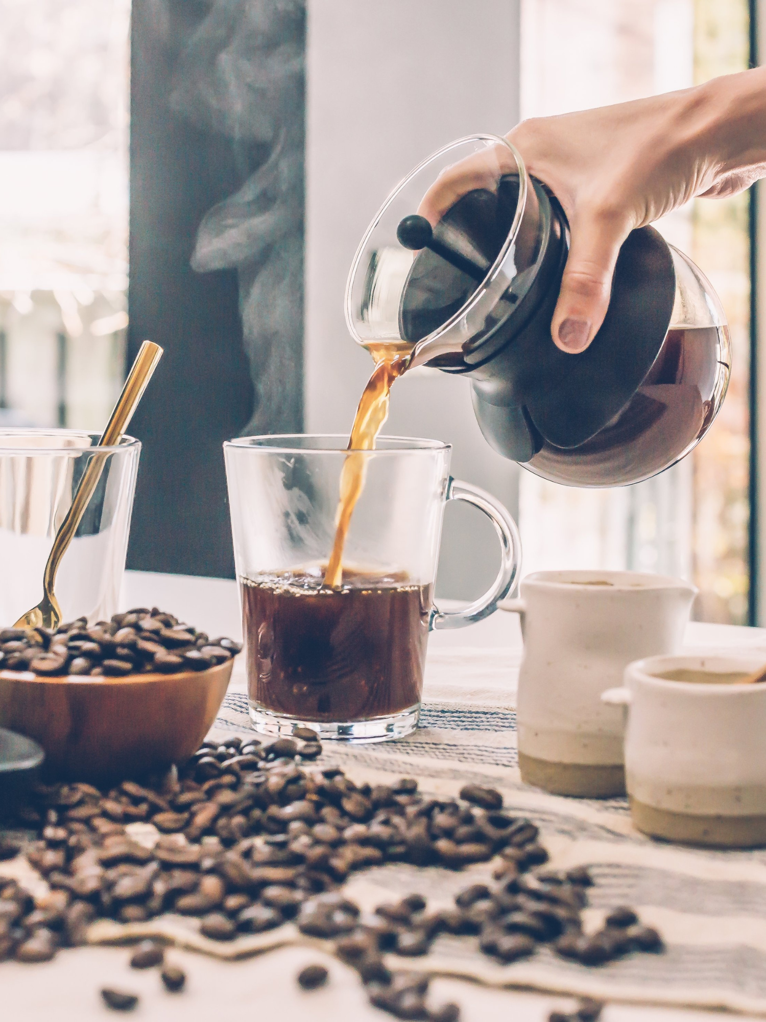 someone pouring a french press of coffee into a clear mug on a table 