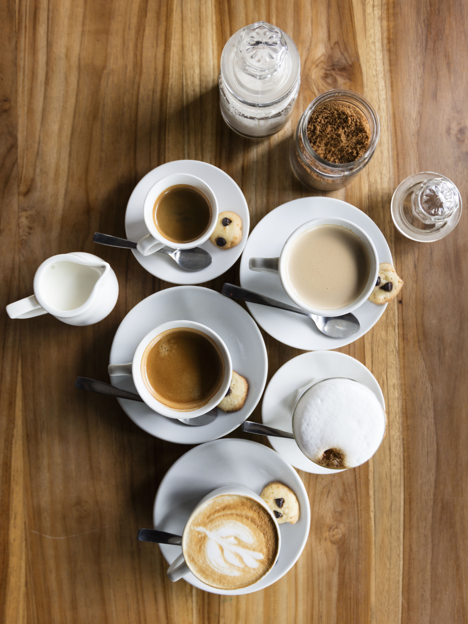 many cups of coffee on saucers sitting on a wooden table