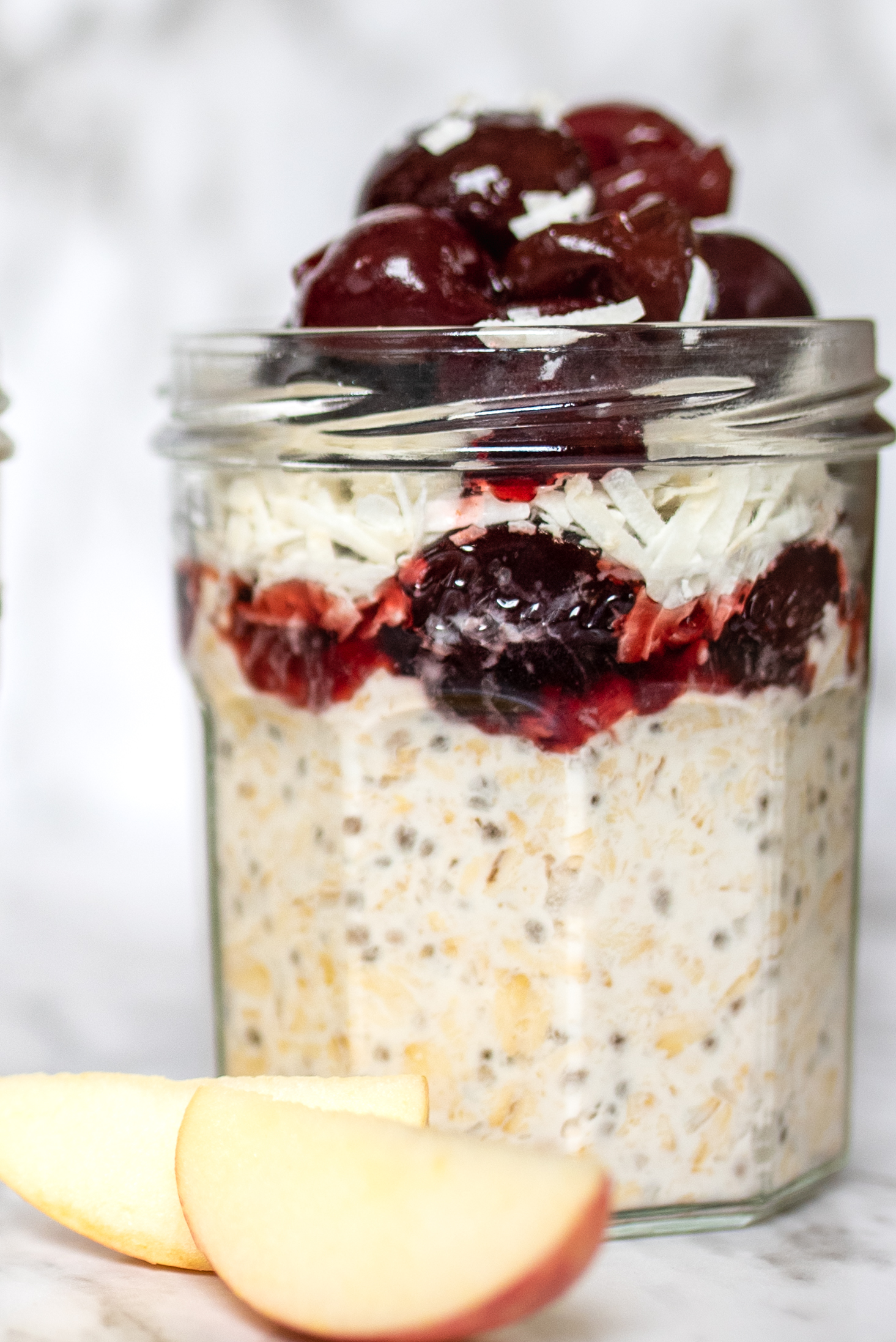 A Jar of almond, cherry, coconut overnight oats with two apple slices in front