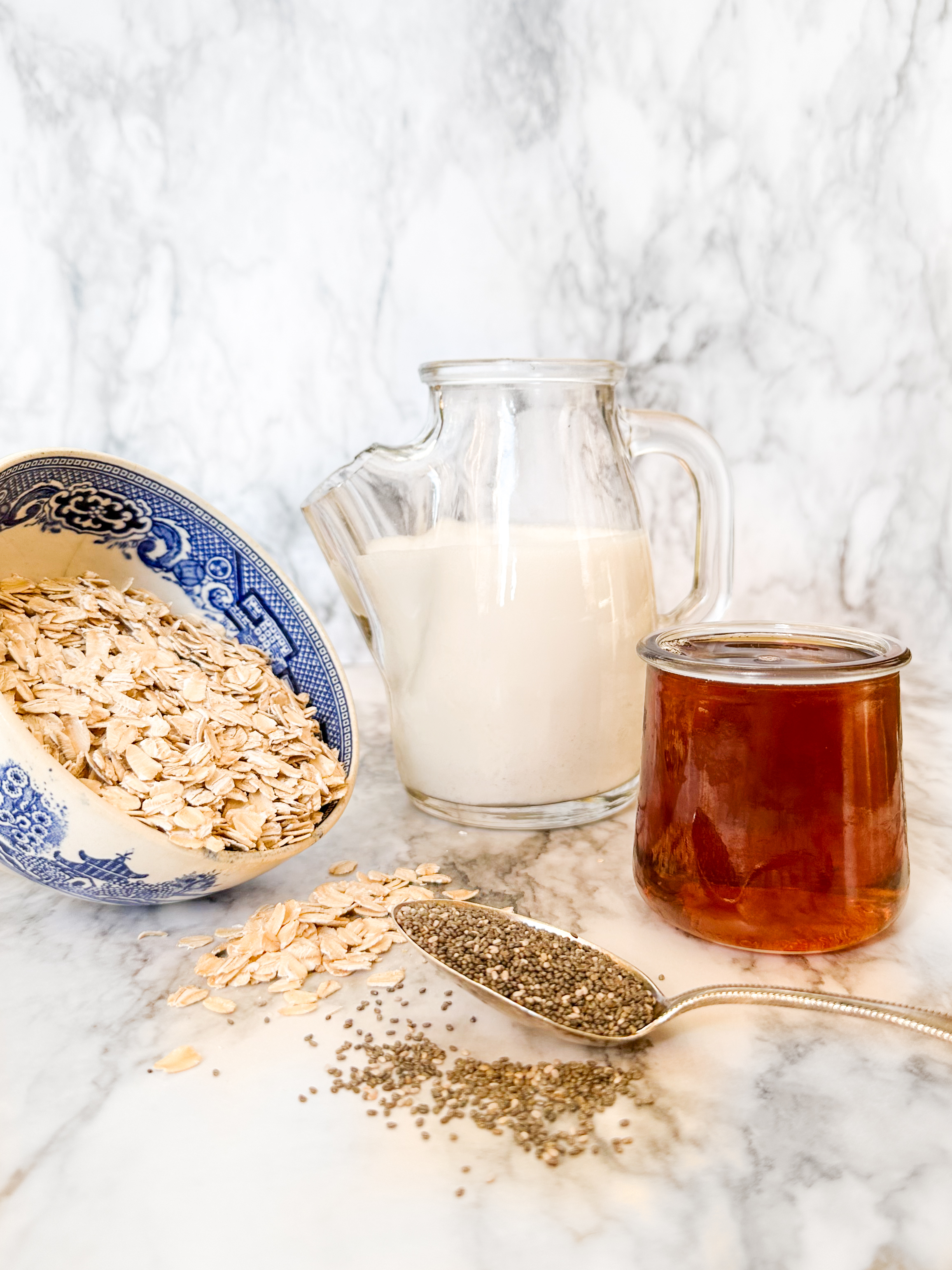 Ingredients for coconut milk overnight oats including a bowl of gluten free oats a spoonful of chia seeds and pitcher of coconut milk and a small jar of maple syrup