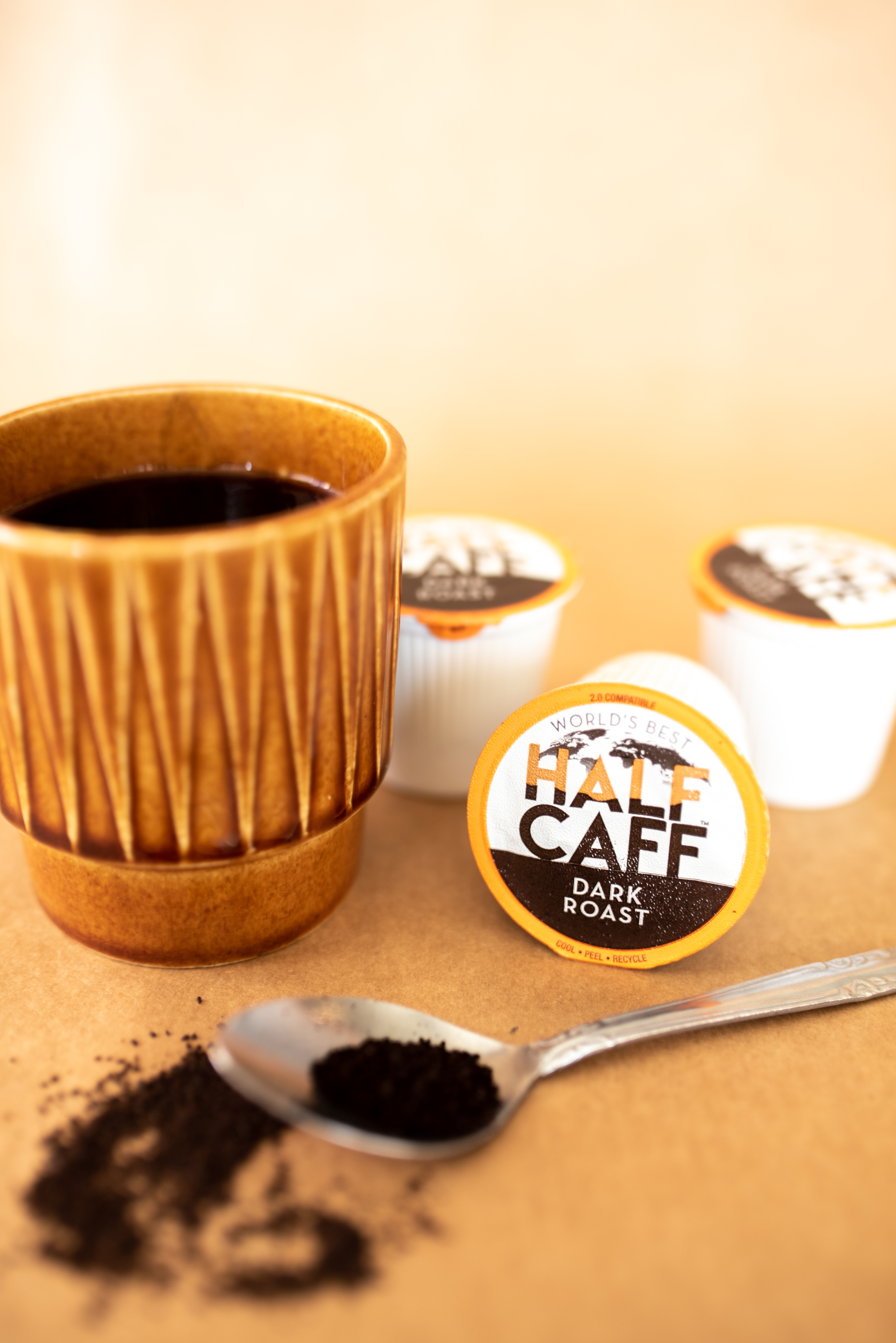 a brown cup with dark liquid inside sitting next to a spoon of coffee grounds