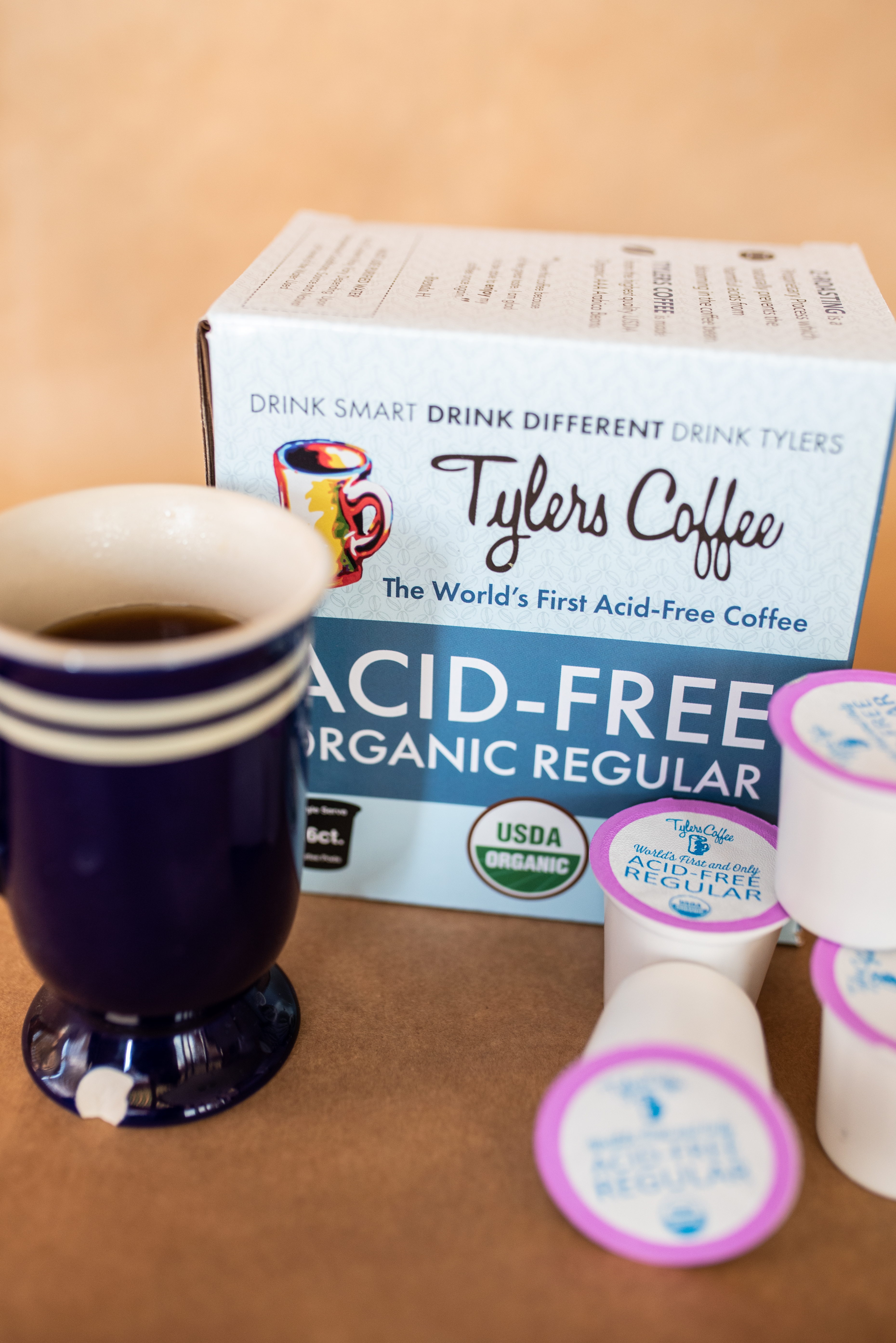 a blue mug in front of a box of coffee pods sitting on a brown table